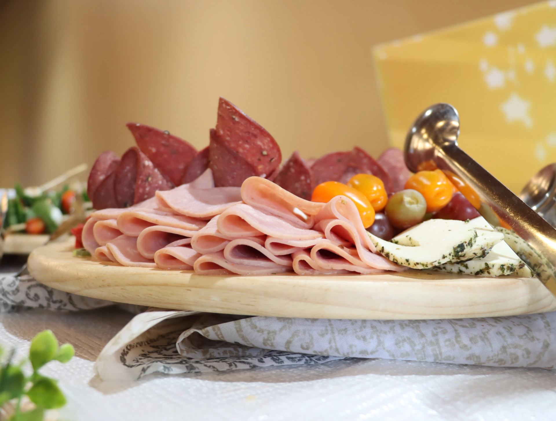 Charcuterie board with sliced deli meats, herbed cheese, olives and small peppers.