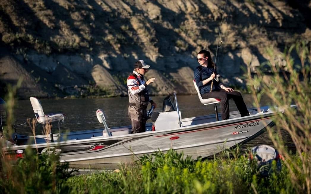 Fishing boat with two anglers casting lines on a river near rocky hillsides.