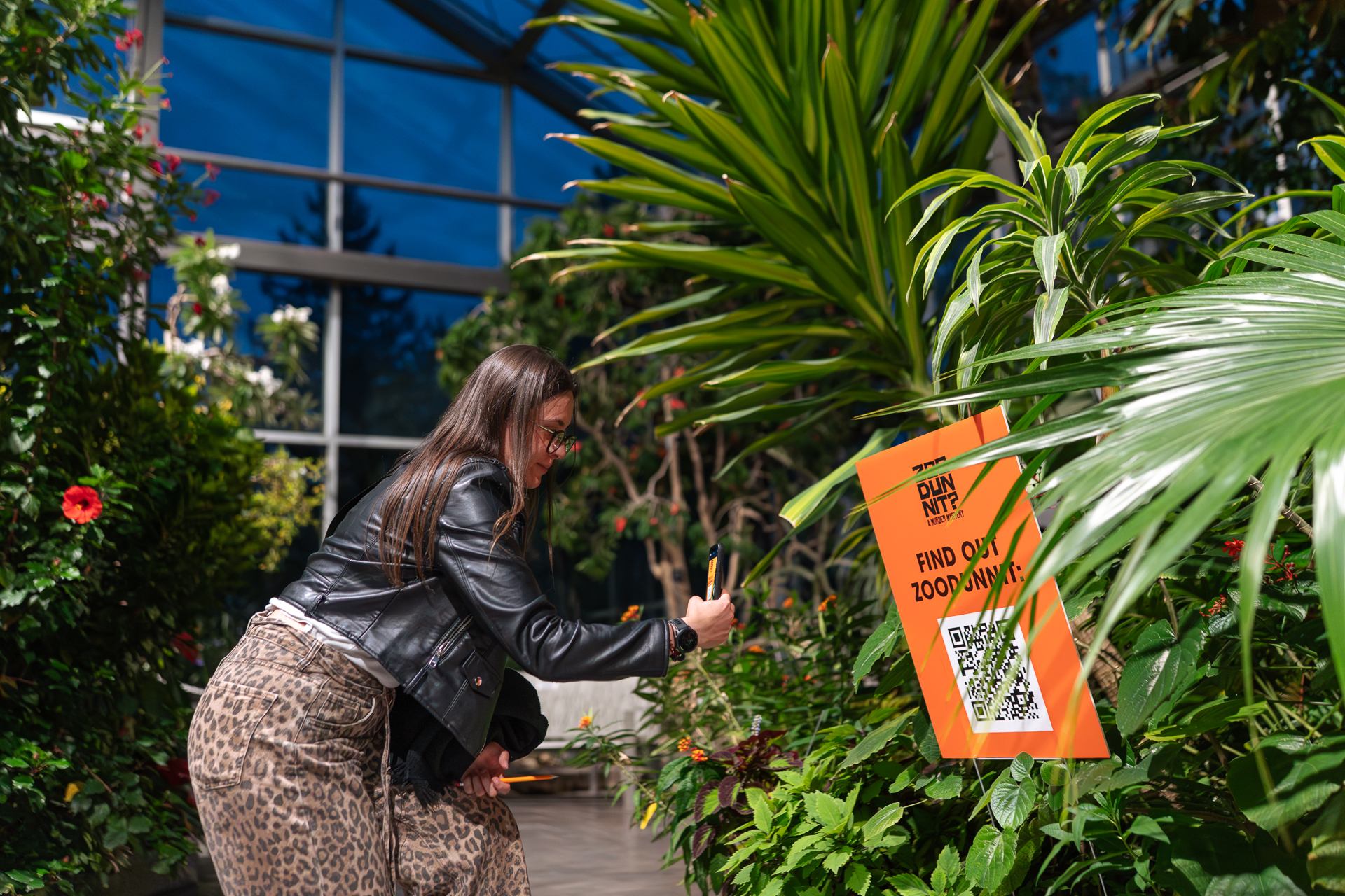 Visitor scans a QR code on an orange sign among tropical plants.