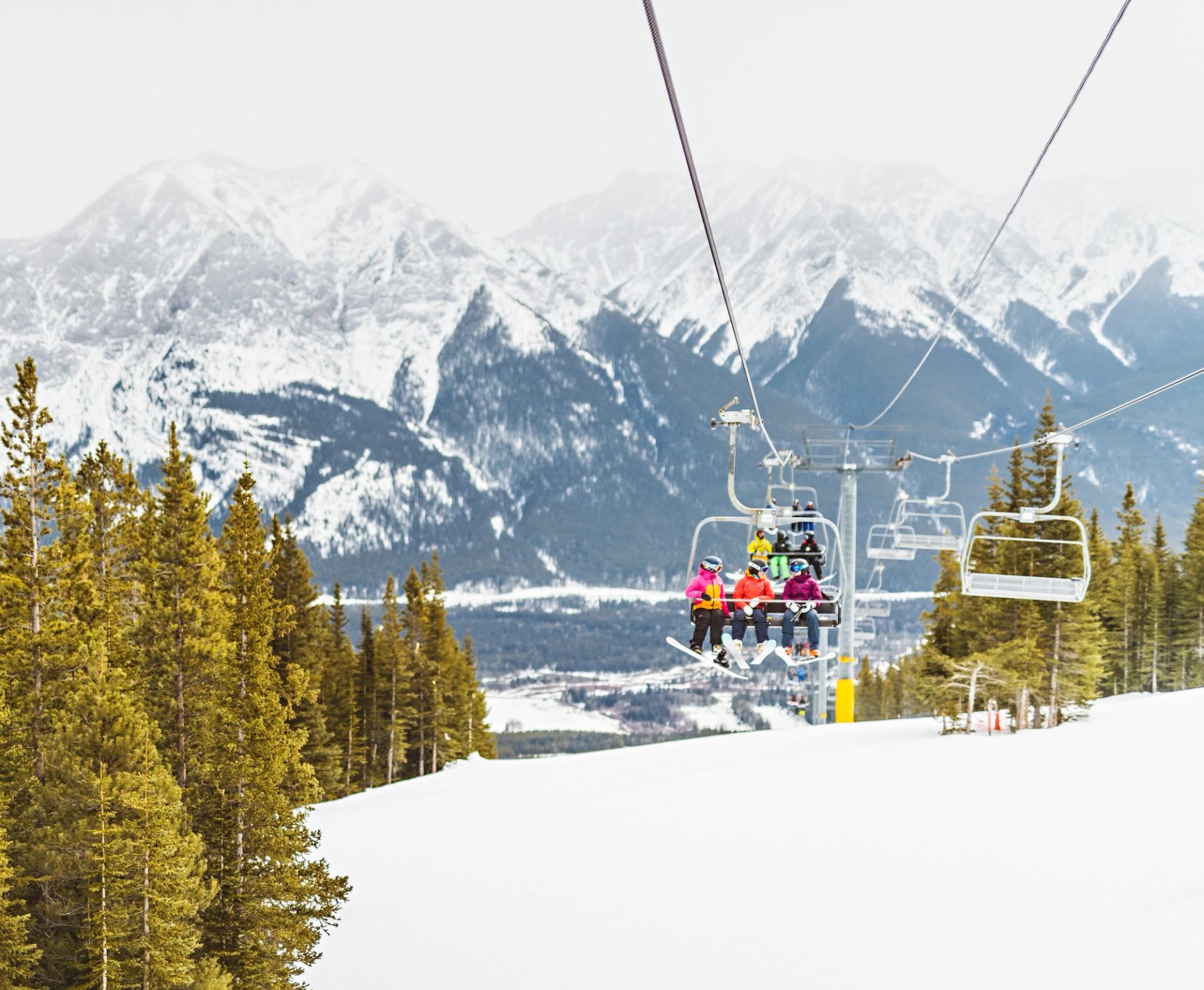 Friends taking the chairlift at Nakiska, with a beautiful mountain range in the background in Kananaskis Country