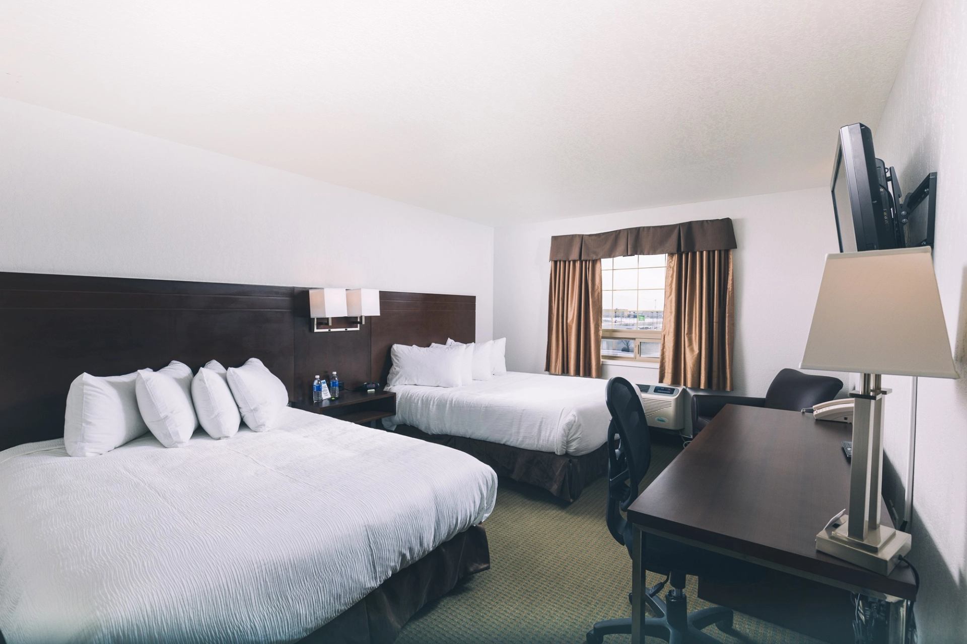 Hotel room with two beds, desk, chair, lamp, TV and window.