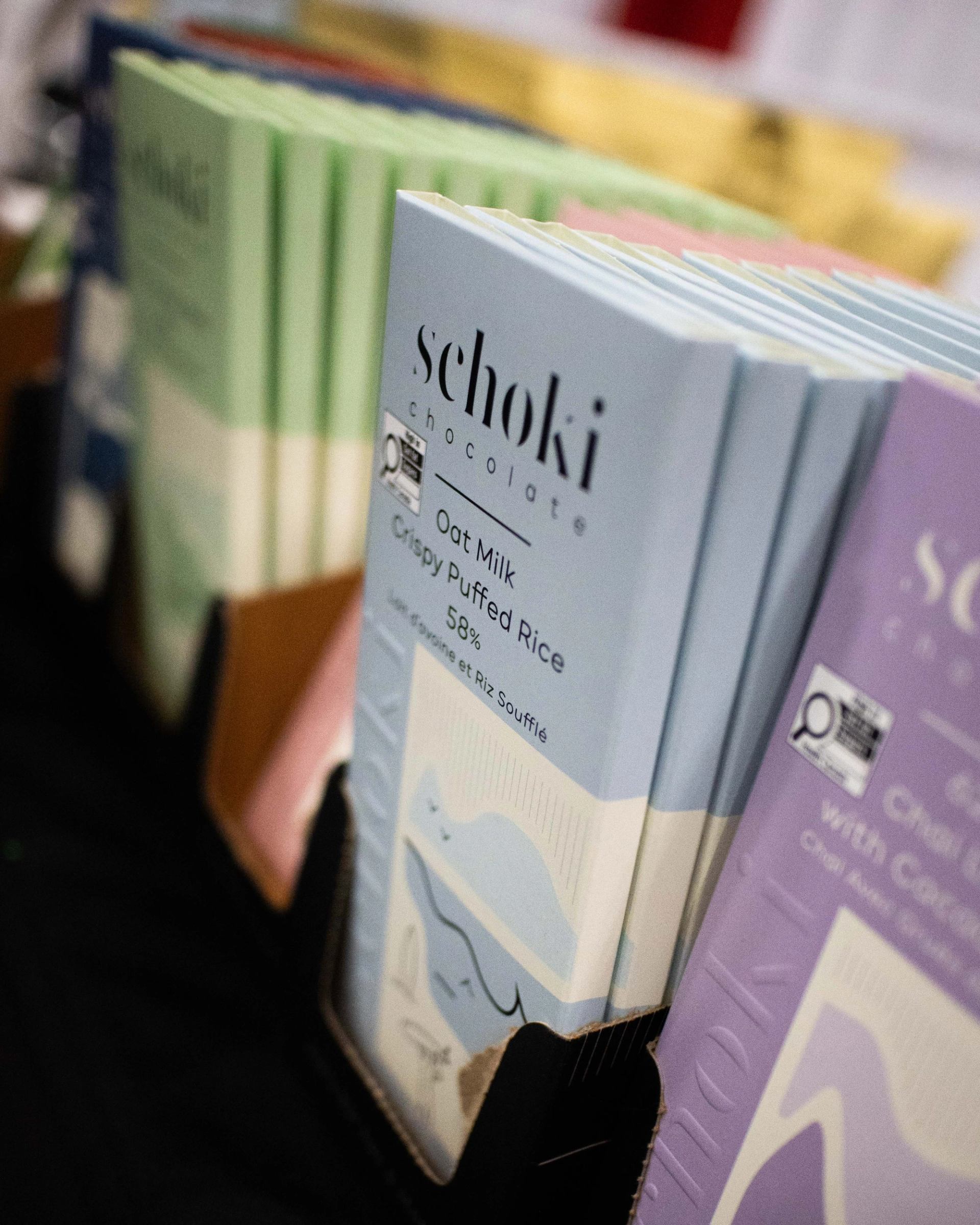 Display of Schoki chocolate bars in pastel wrappers standing upright in cardboard holders.