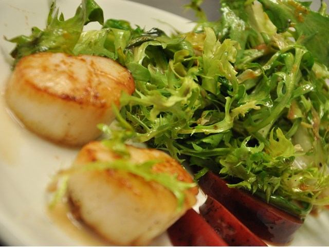 Seared scallops with fresh greens and roasted red peppers, plated artfully.