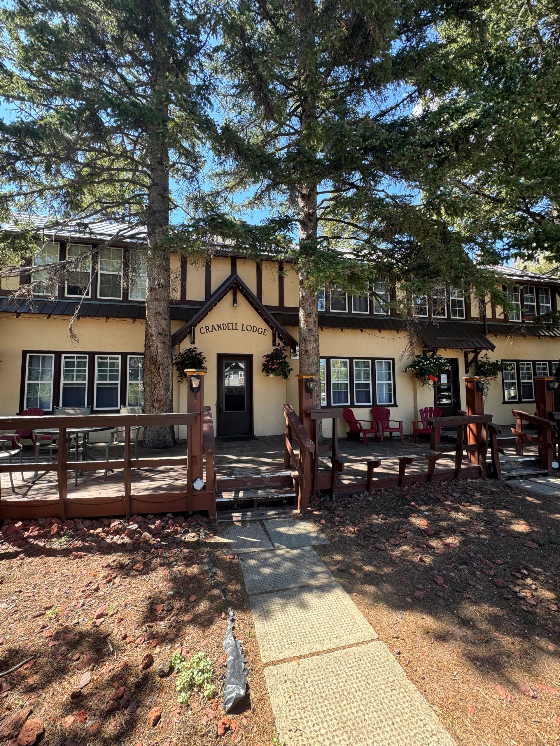 Rustic lodge exterior with trees, fence, and welcoming entrance sign.