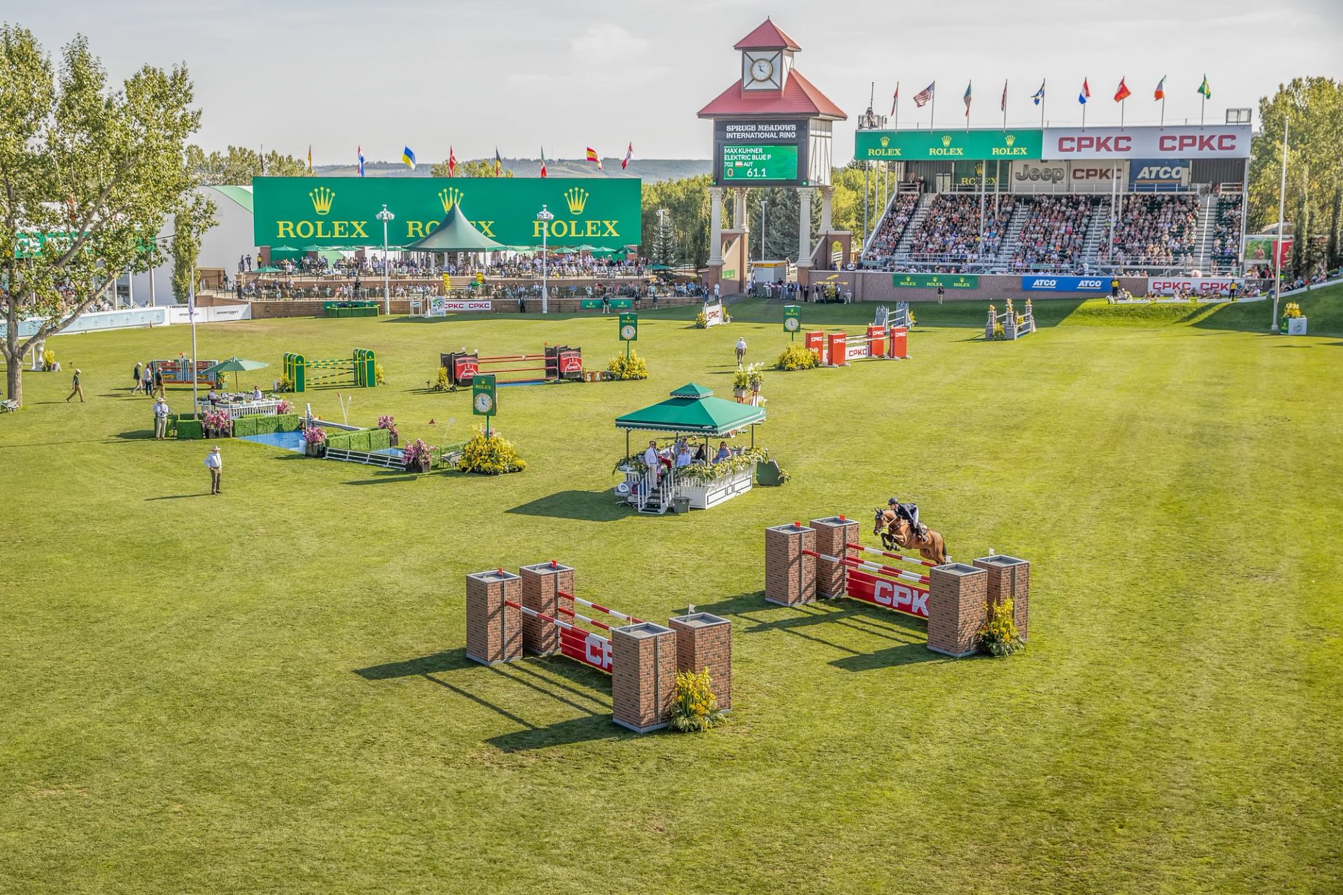 Show jumping course at Spruce Meadows with green field, obstacles, spectators, and grandstands in background.