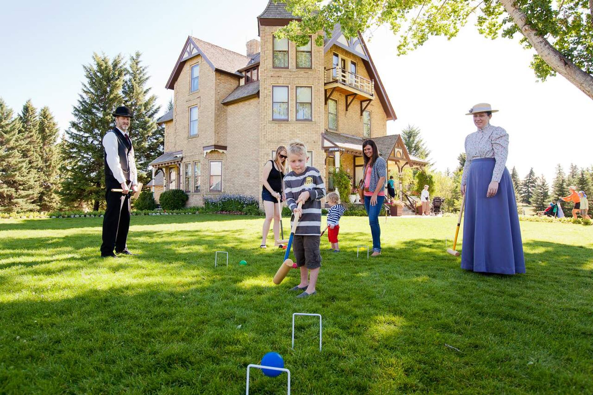 People playing croquet on a lawn in front of a large brick house.