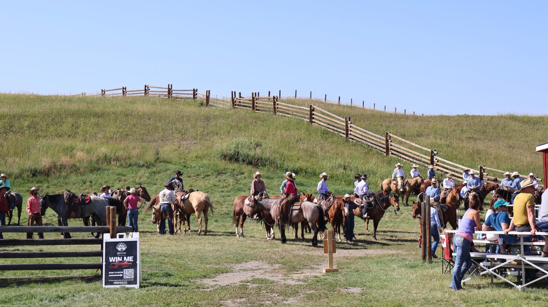 People on horseback gather near wooden fences and hills during an Old Time Ranch Rodeo.