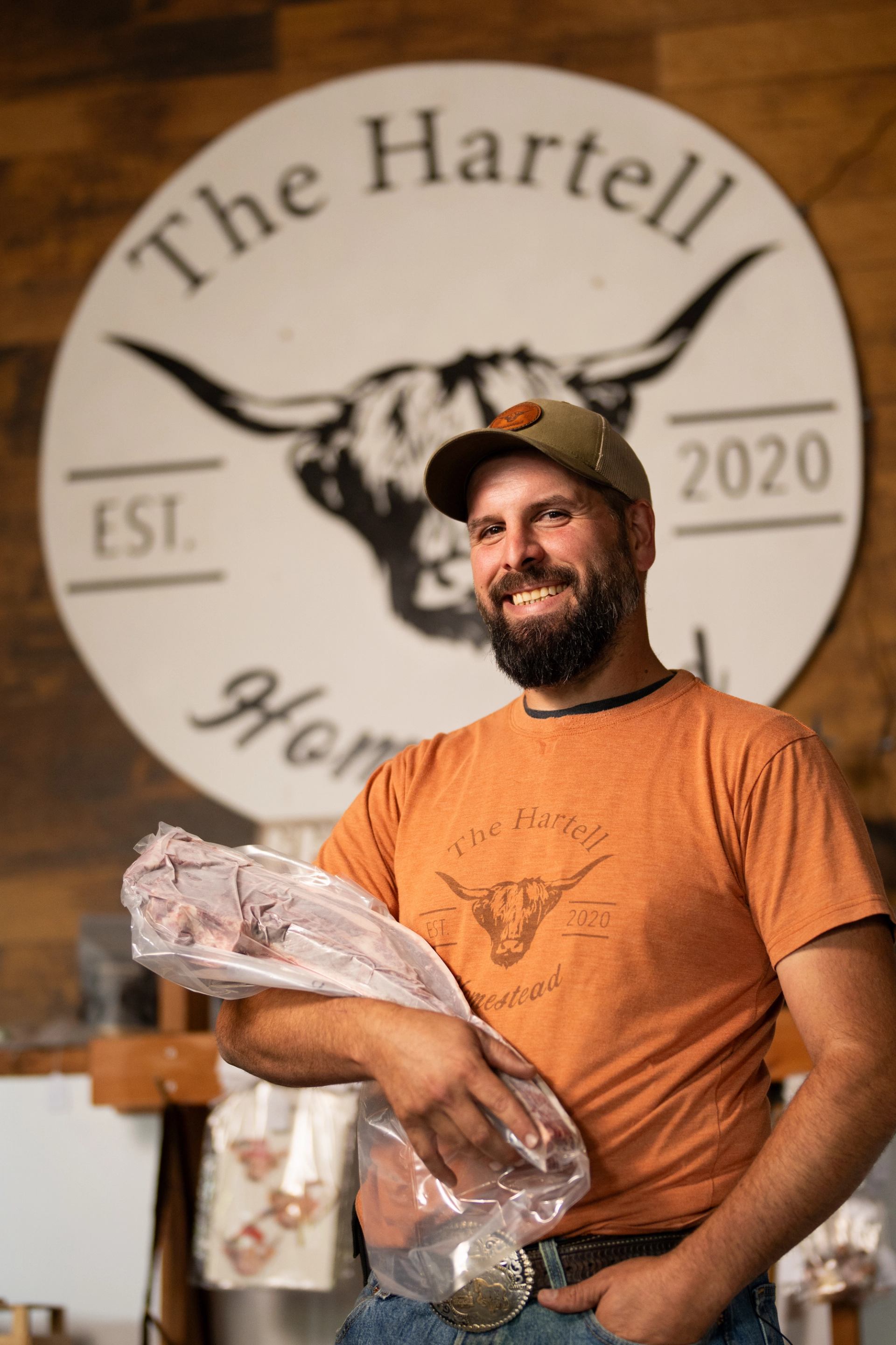 Person holding packaged meat in front of The Hartell Homestead sign.