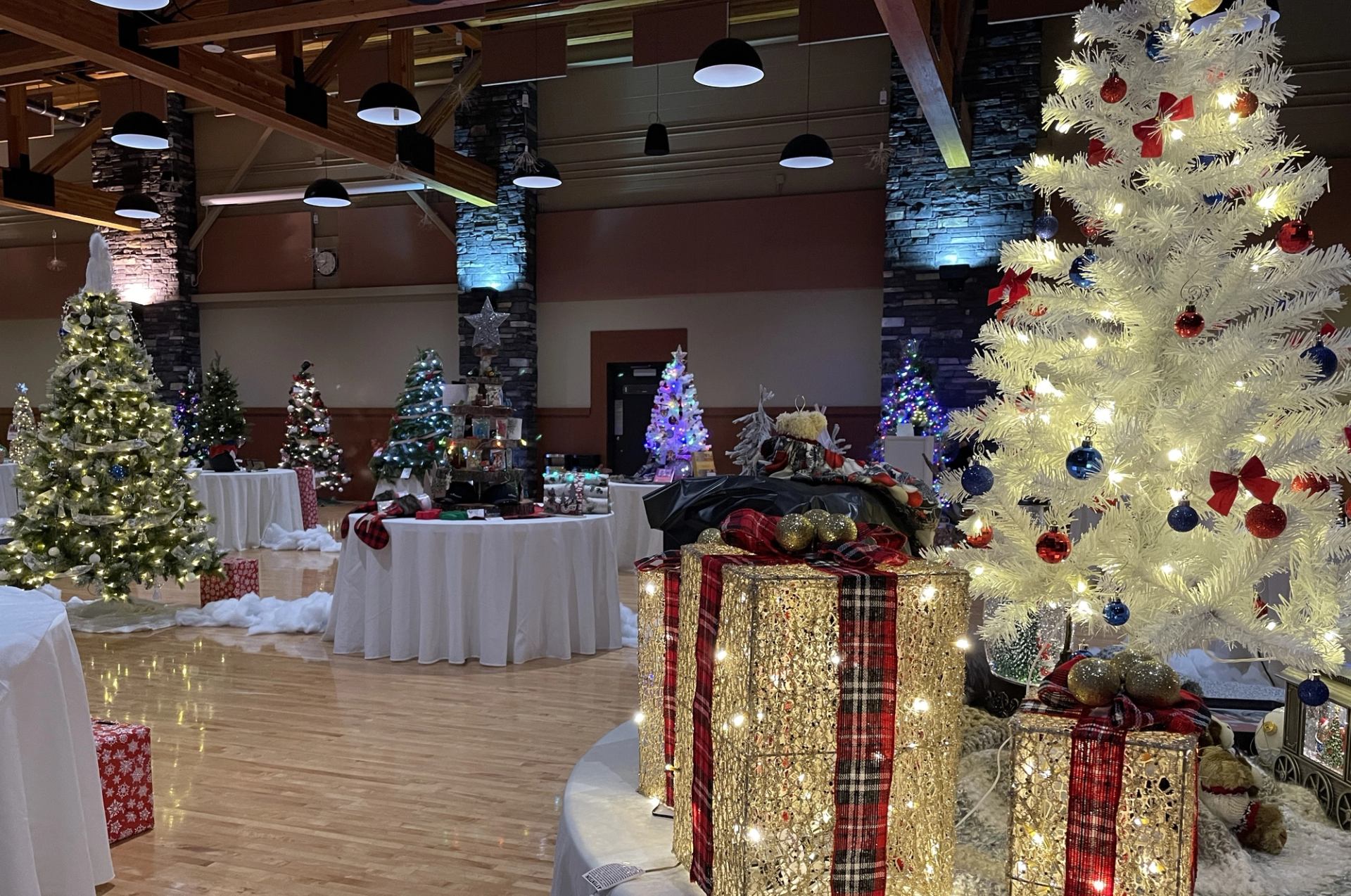 Decorated Christmas trees and wrapped gift displays in an indoor hall, with ornaments and lights.