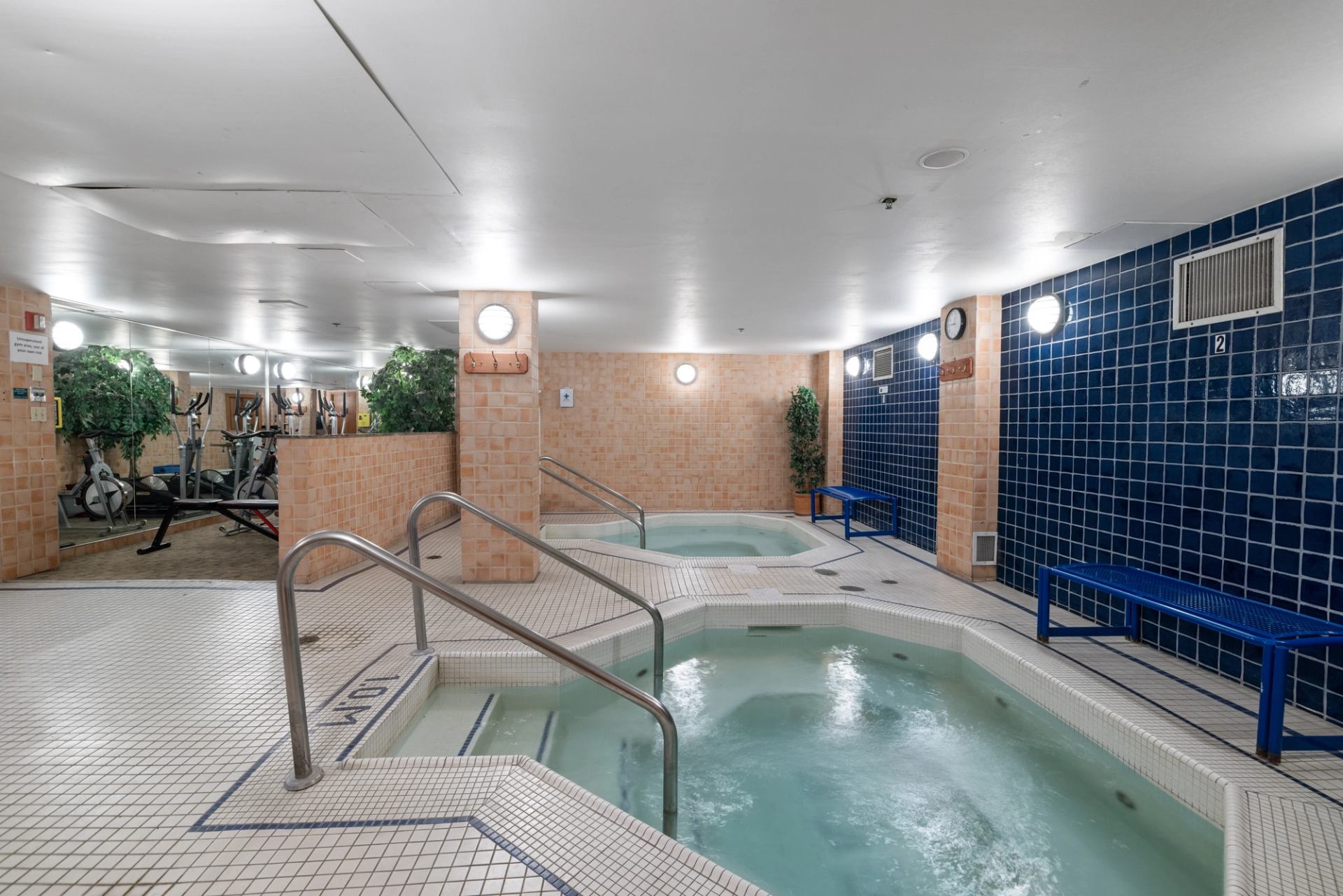 Indoor spa with two hot tubs, tiled walls, and a bench at Banff Ptarmigan Inn.