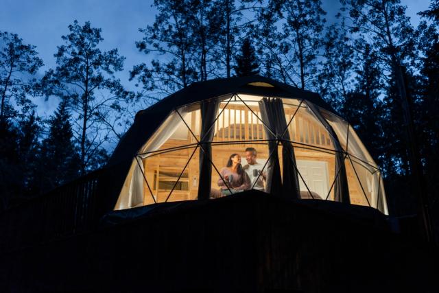 A couple sits together sipping on tea under the stars inside one of the domes at Glamping Resorts in Castle Provincial Park.