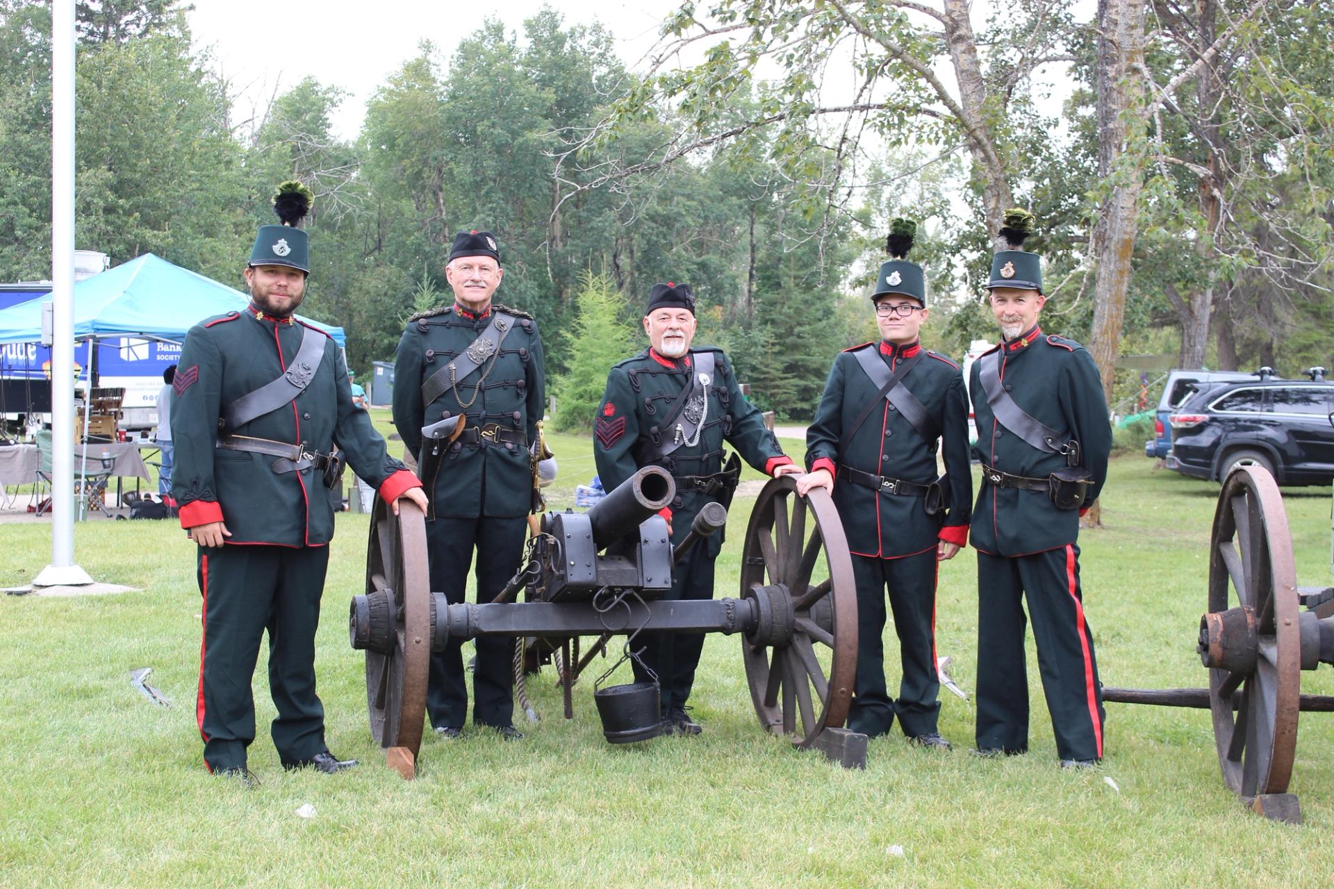 Uniformed historical re-enactors stand beside a cannon on a grassy field.
