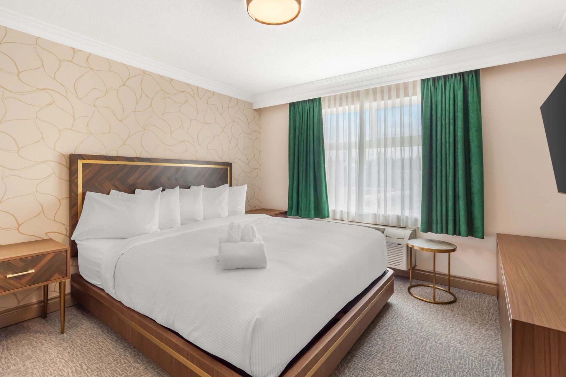 Elegant hotel bedroom with a large bed, crisp white linens, green curtains, and modern wooden furniture.