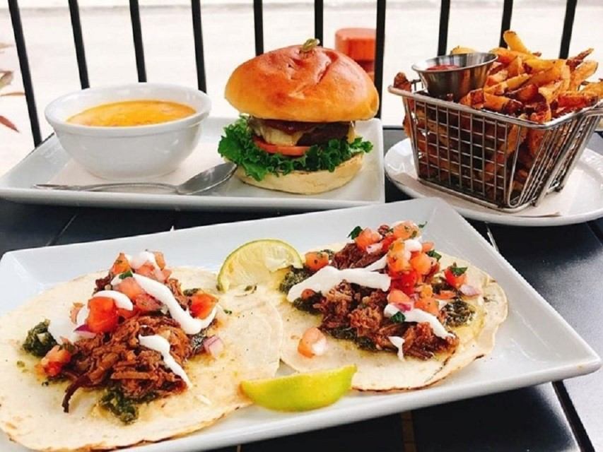 Tacos, burger, fries, and soup served on a patio table at Tavern 1883.