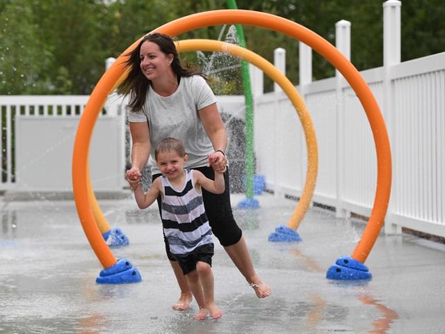 A mother holds the hands of young child as they play in a splash park.