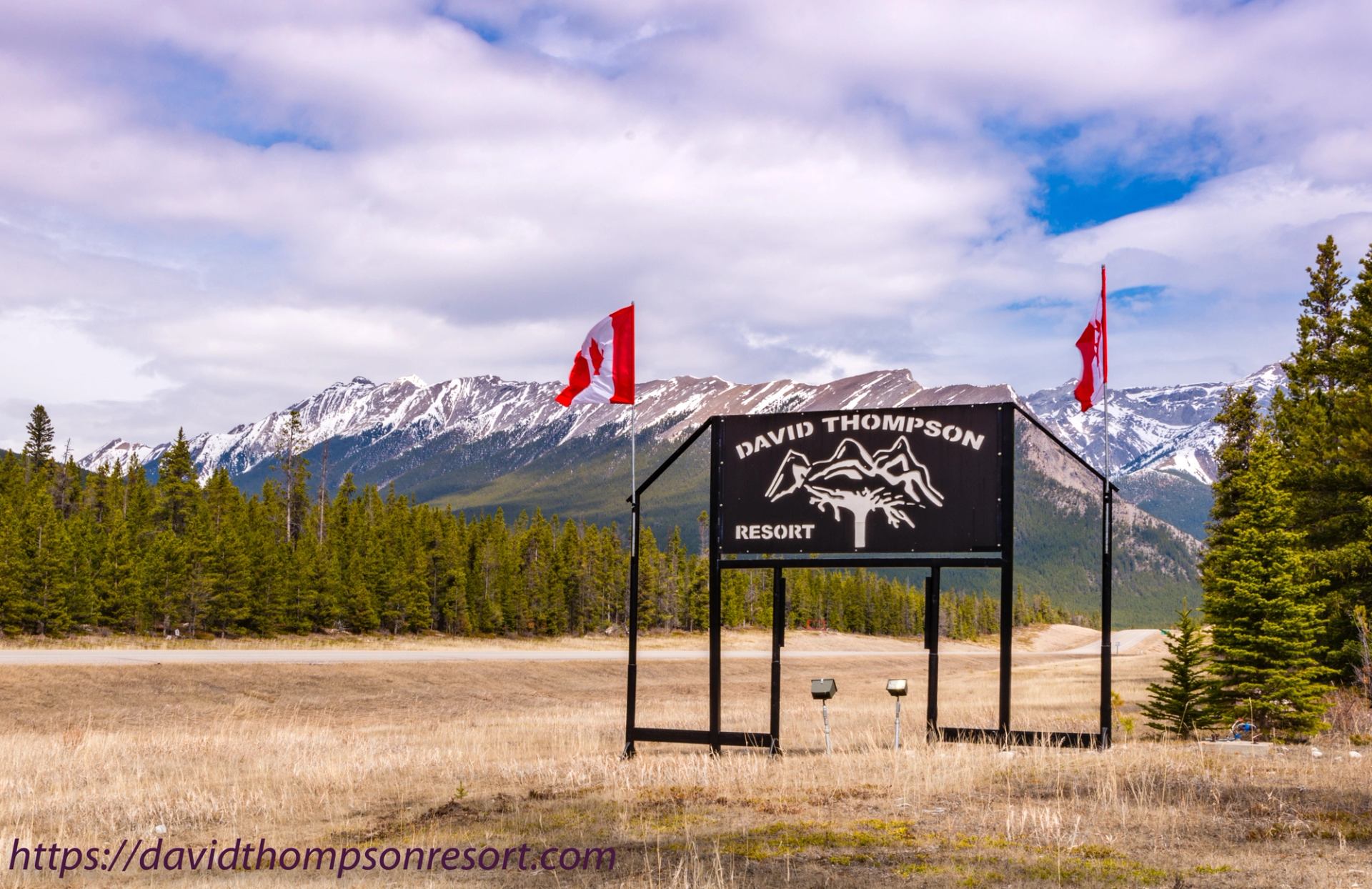 David Thompson Resort sign and Canadian flags stand before snow-capped mountains.