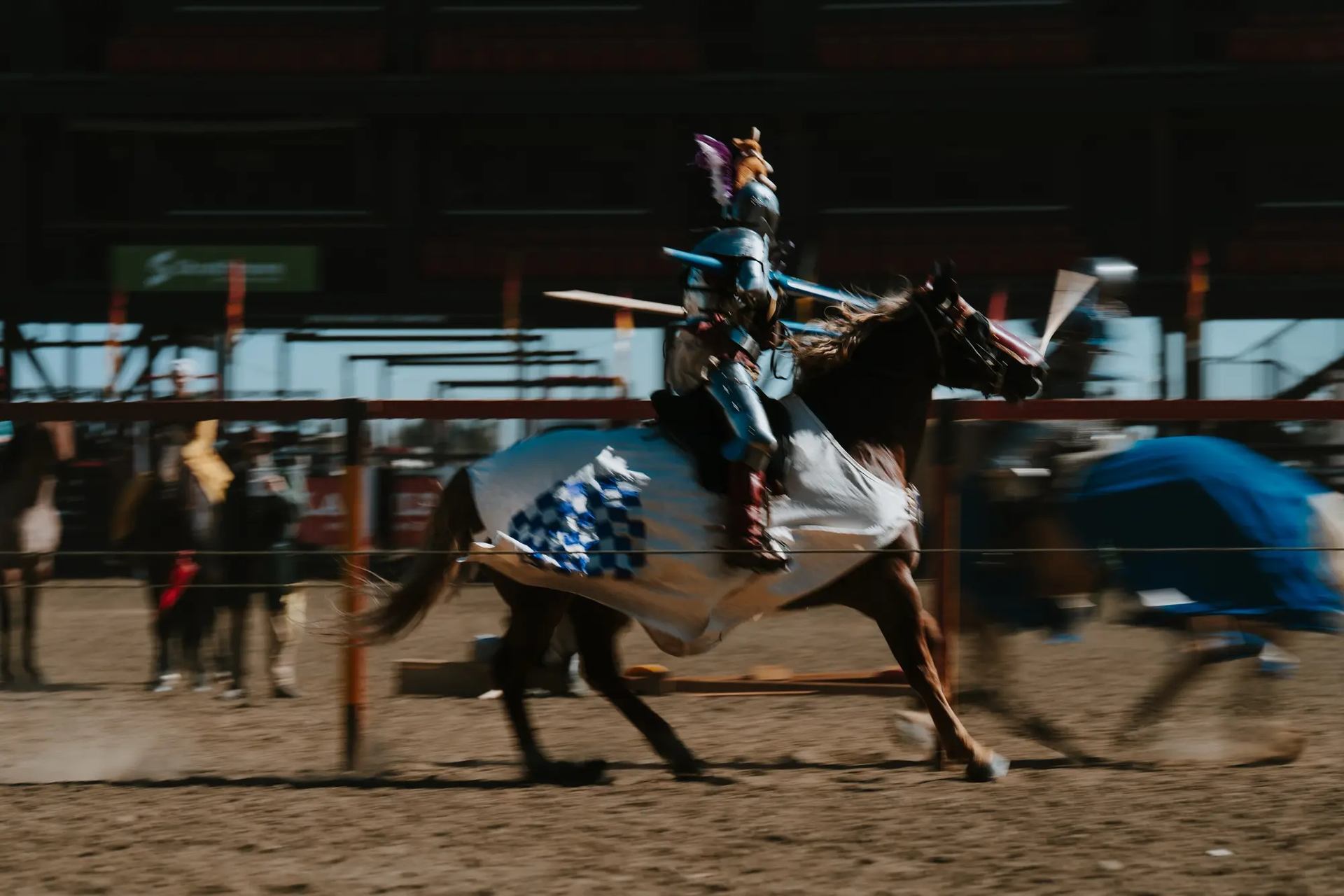Armored jouster on horseback at Strathmore Medieval Faire with spectators in the background.