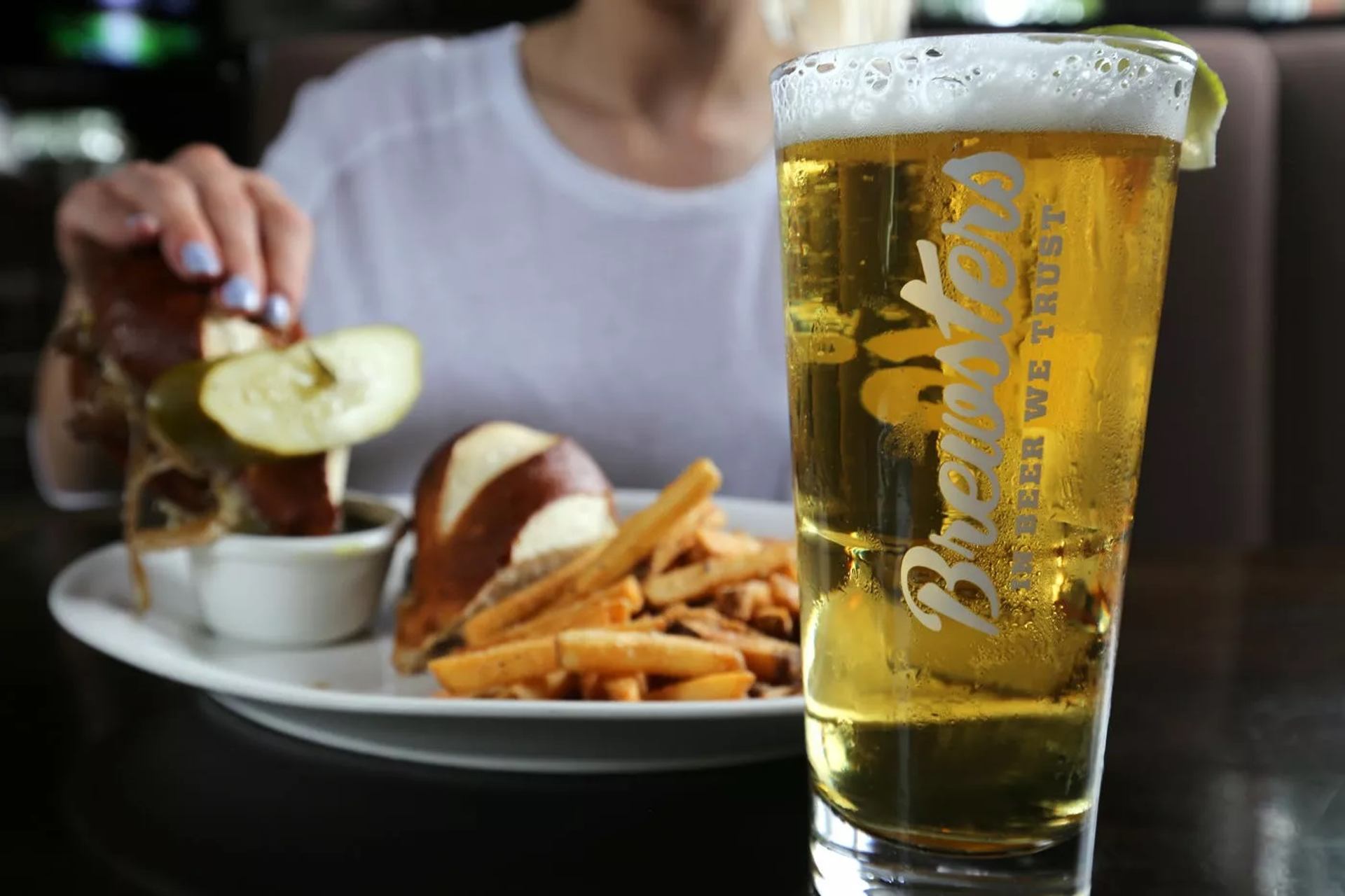 A chilled Brewsters beer stands beside fries and a sandwich served on a restaurant table.