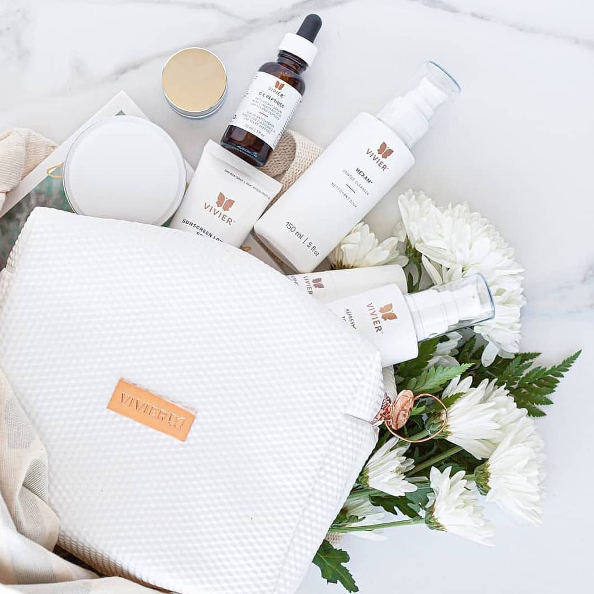 Vivier skincare bottles and jars arranged beside white cosmetic bag and flowers.
