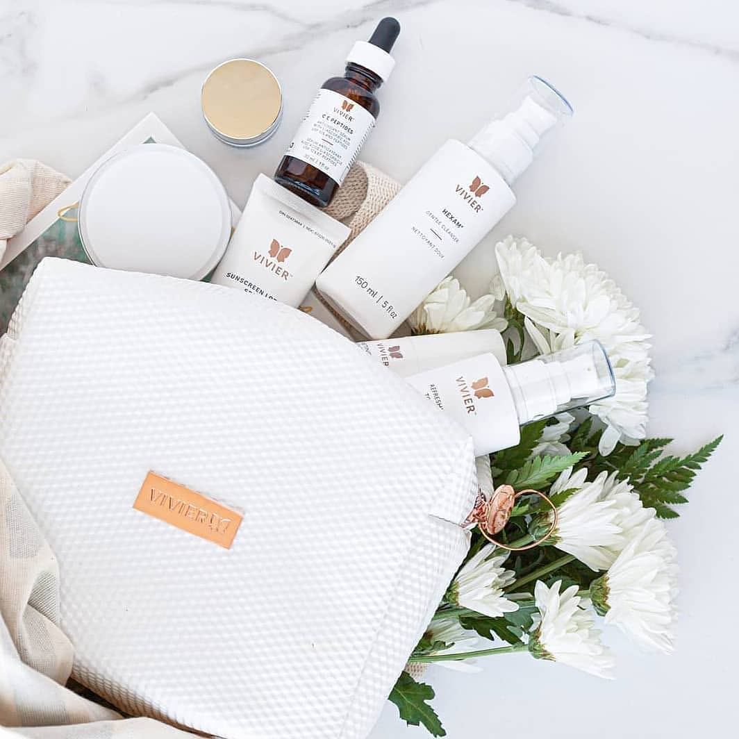 Vivier skincare bottles and jars arranged beside white cosmetic bag and flowers.