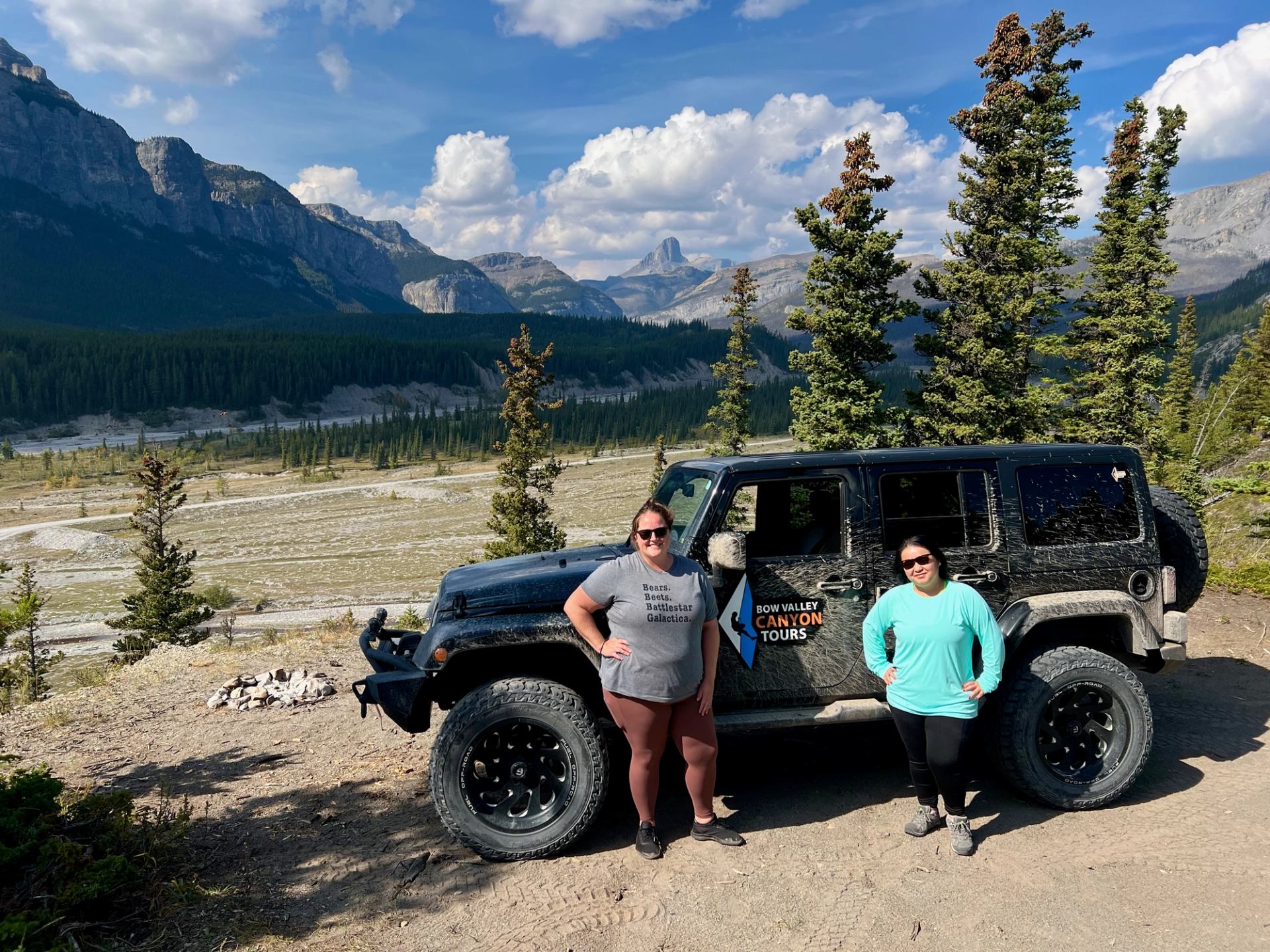 Two people stand beside a black Jeep on a scenic mountain trail.