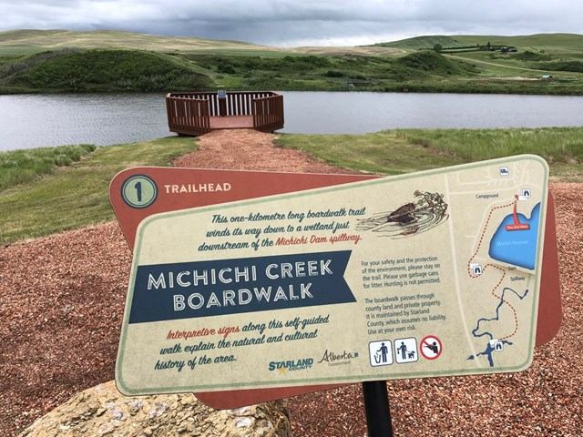 Trailhead sign for Michichi Creek Boardwalk with map and scenic wetland view.