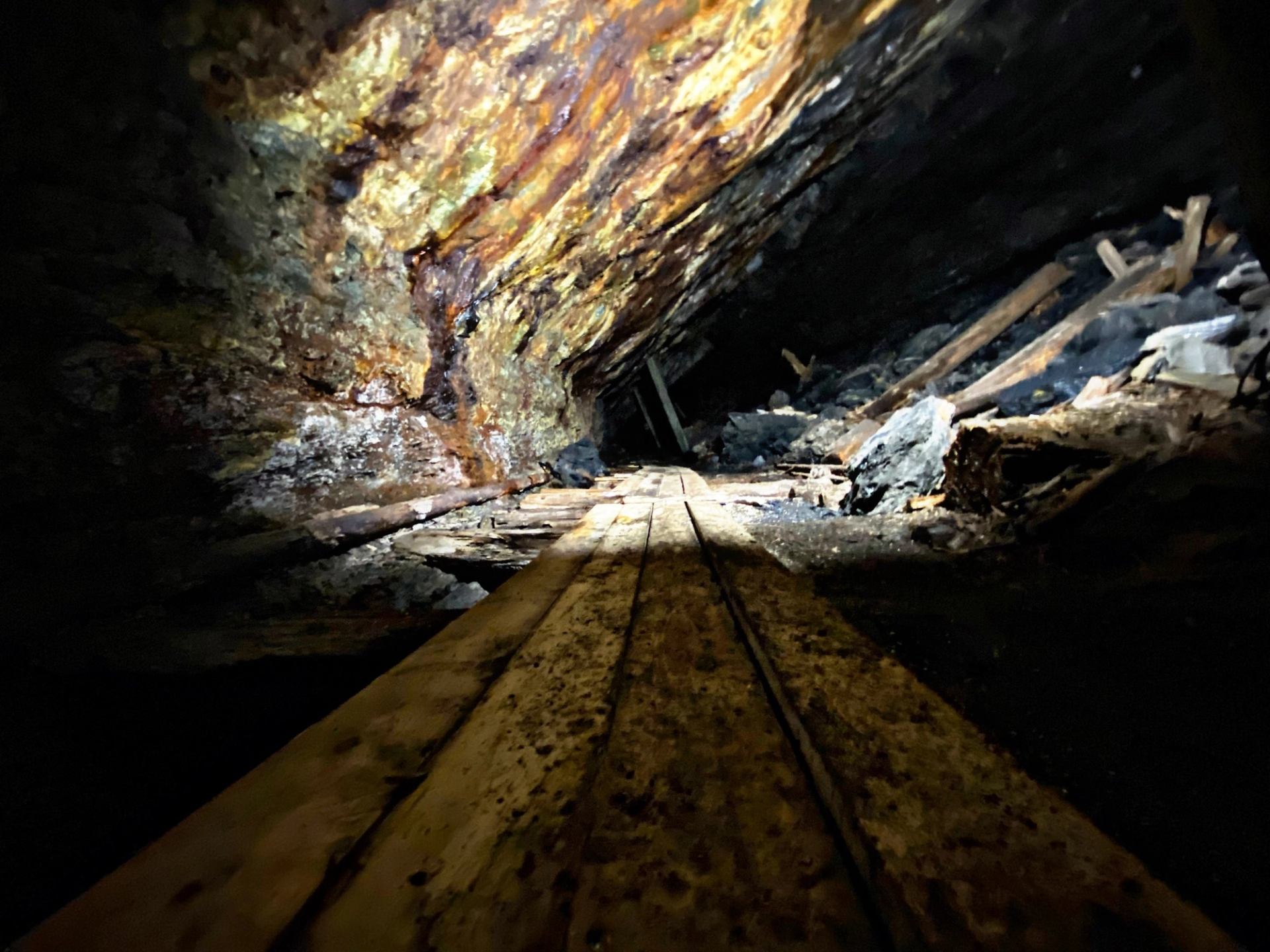 Cave walkway with wooden beams and illuminated rock wall, with metal rails.