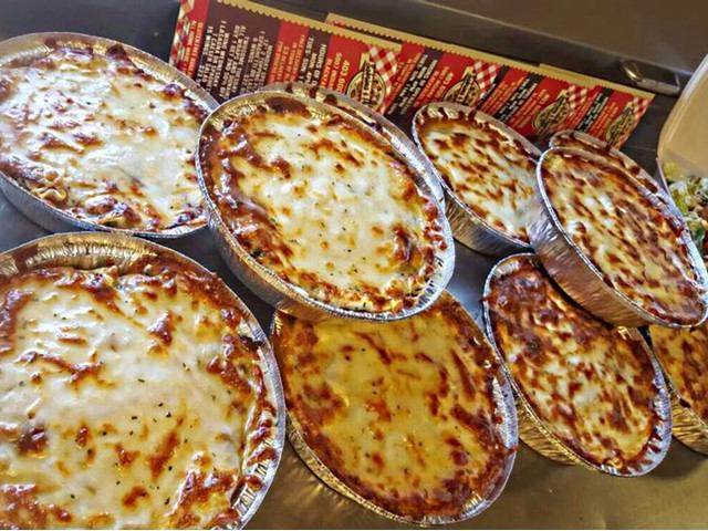 Foil trays of baked lasagna with golden melted cheese on top.