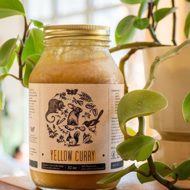 Jar of yellow curry with illustrated label nestled among green leafy plants.