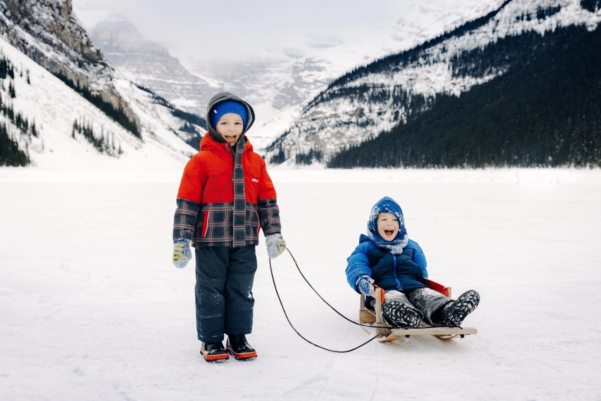 Two children enjoying sledding on a snowy mountain landscape.