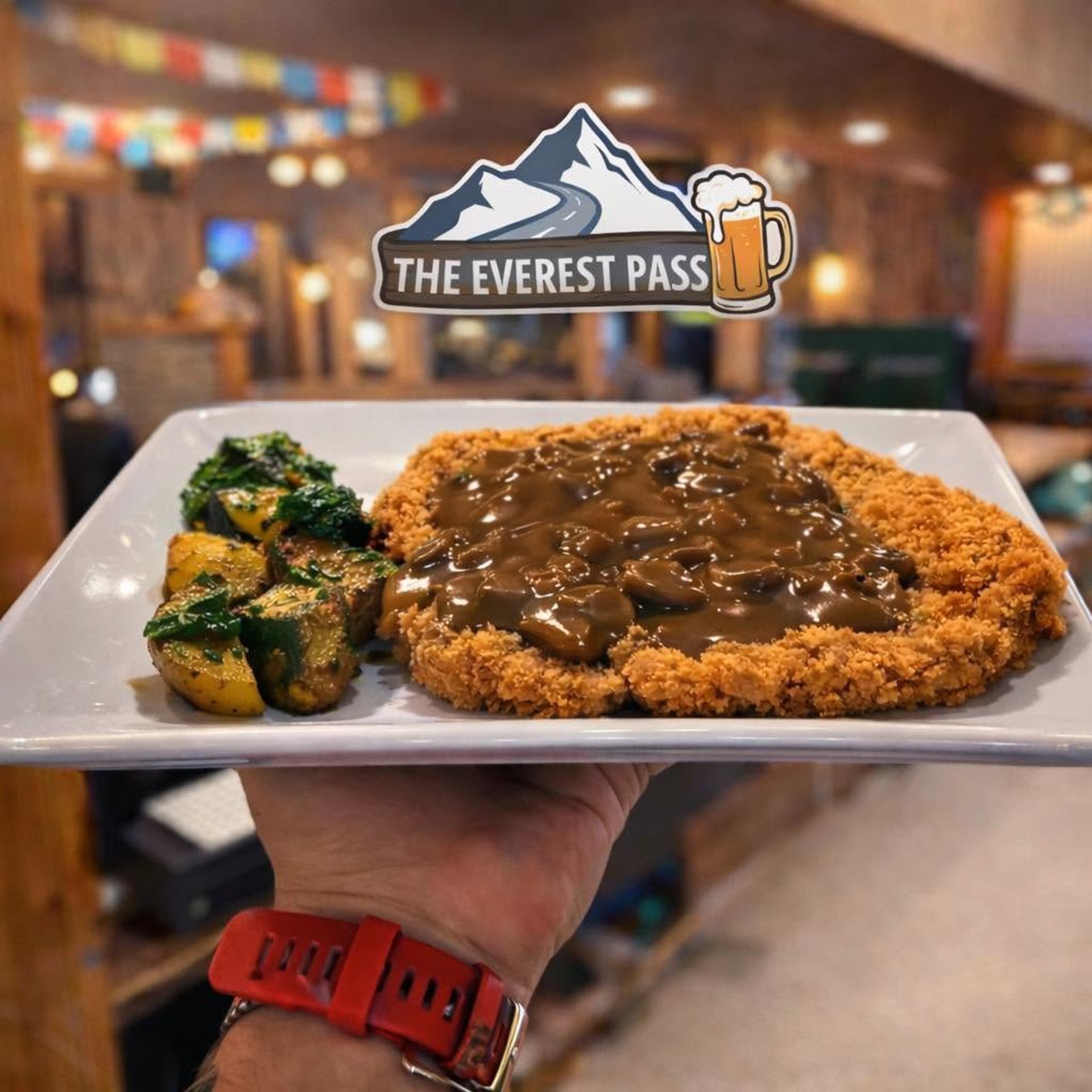 A breaded schnitzel topped with mushroom gravy is served with roasted potatoes and vegetables.