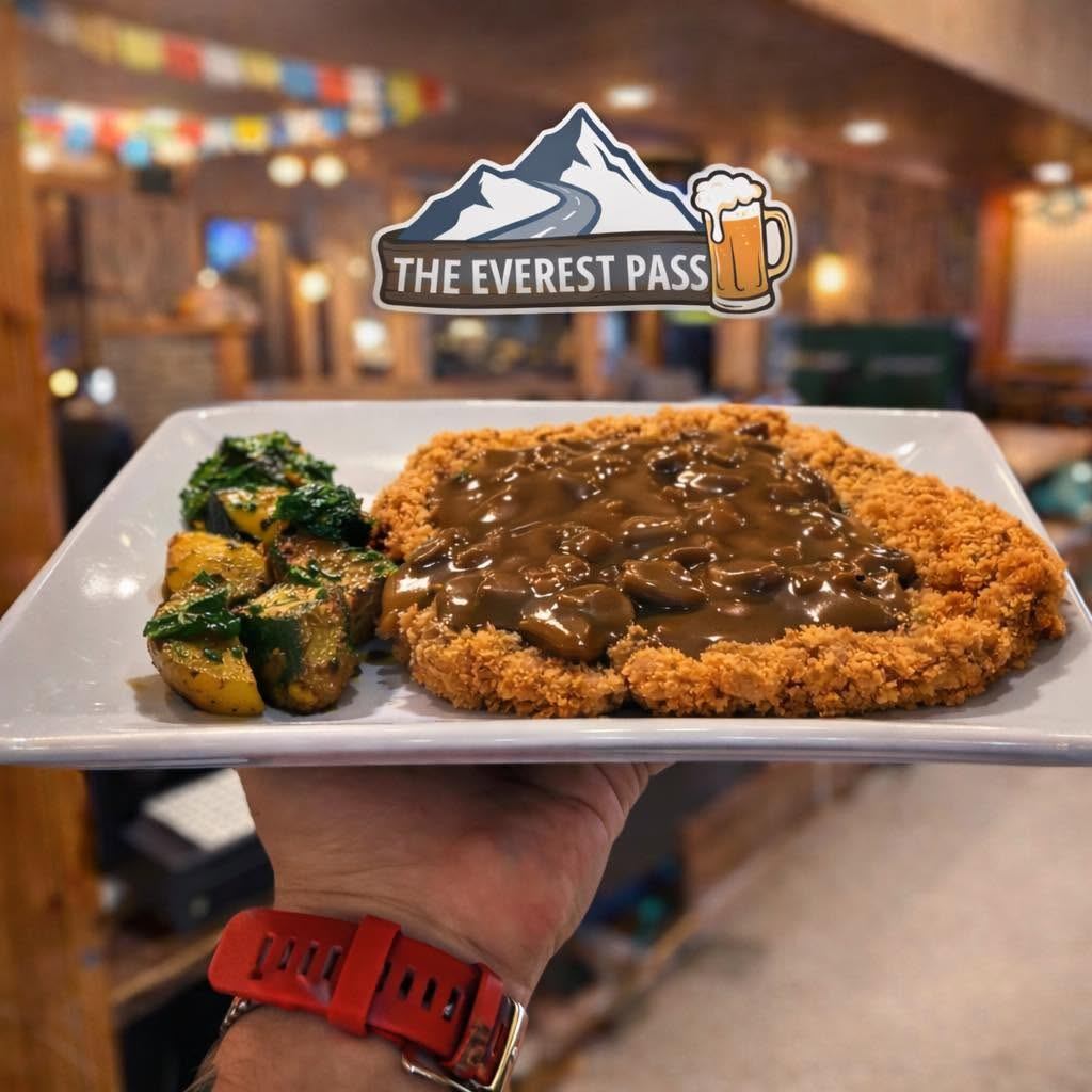 A breaded schnitzel topped with mushroom gravy is served with roasted potatoes and vegetables.