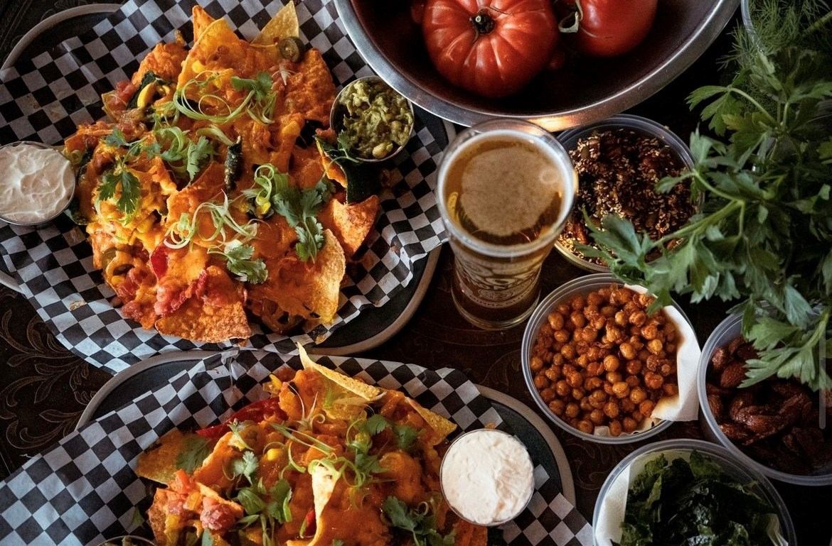 Pizza slices, garlic bread, and bowls of olives and chickpeas on a checkered tablecloth.