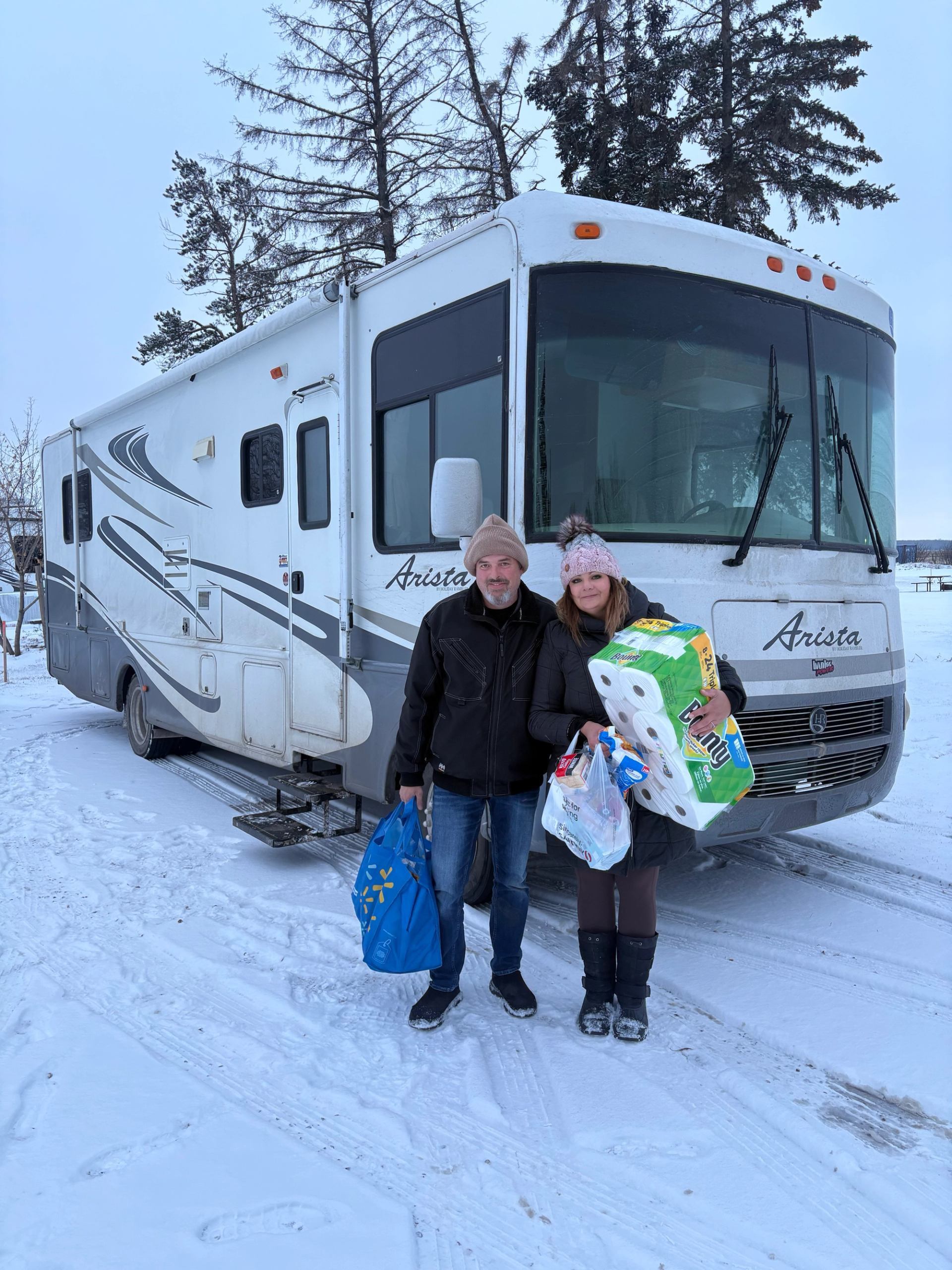 Two people standing by an RV in snowy Lamont RV Park with supplies.