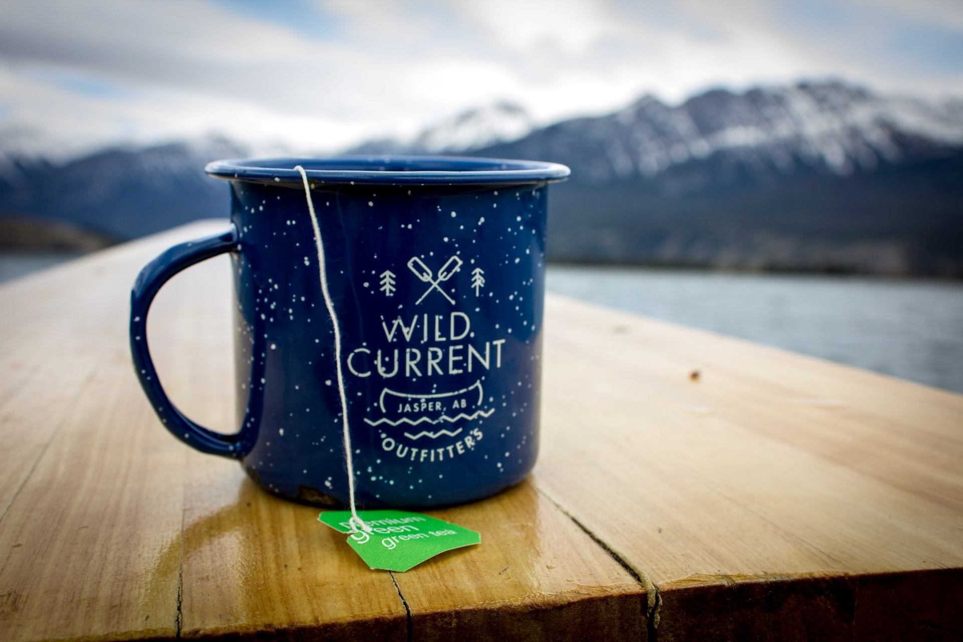 Blue camping mug with paddles logo and mountain lake view at Wild Current.