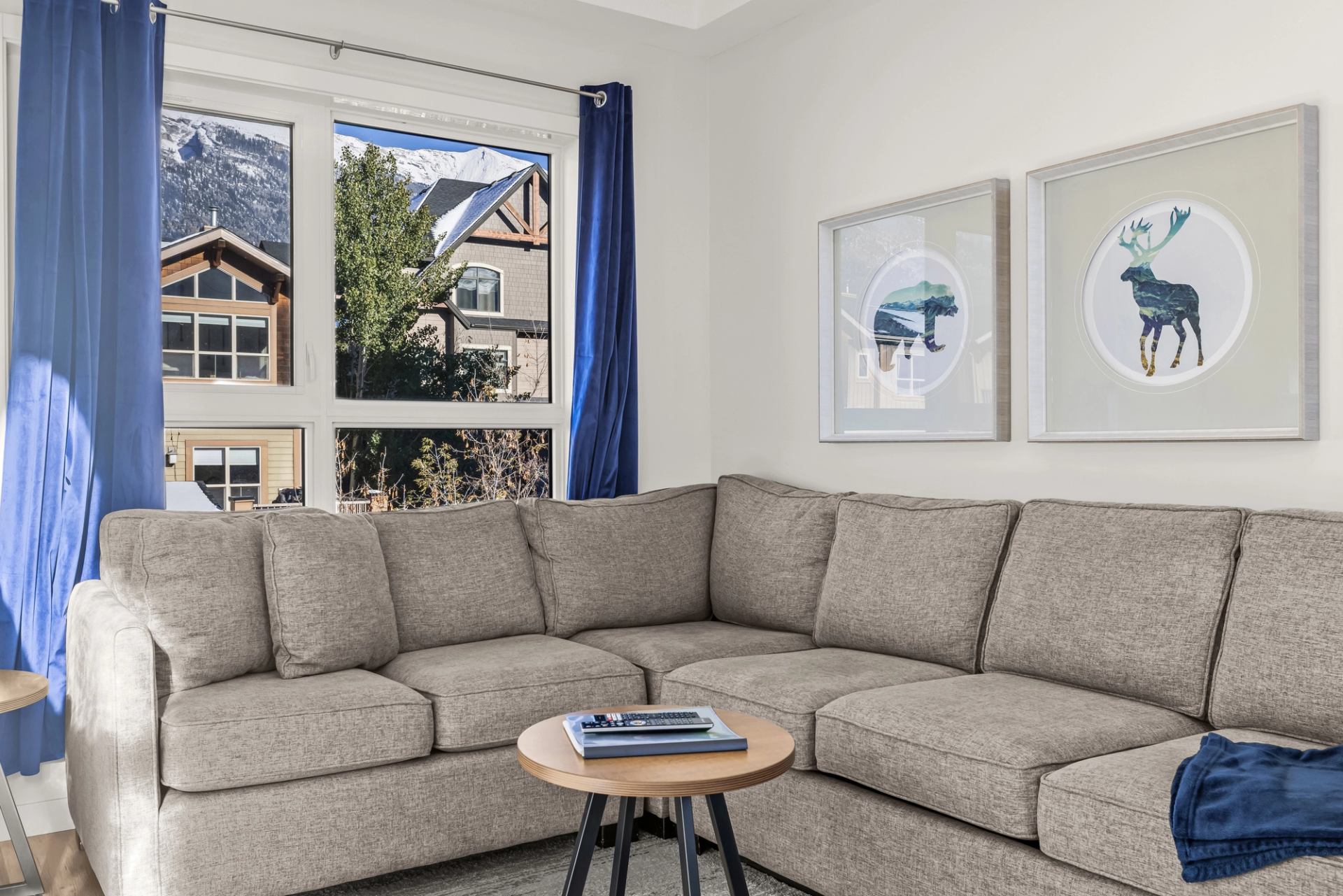 Living room with grey sectional, blue curtains, animal prints and mountain views.