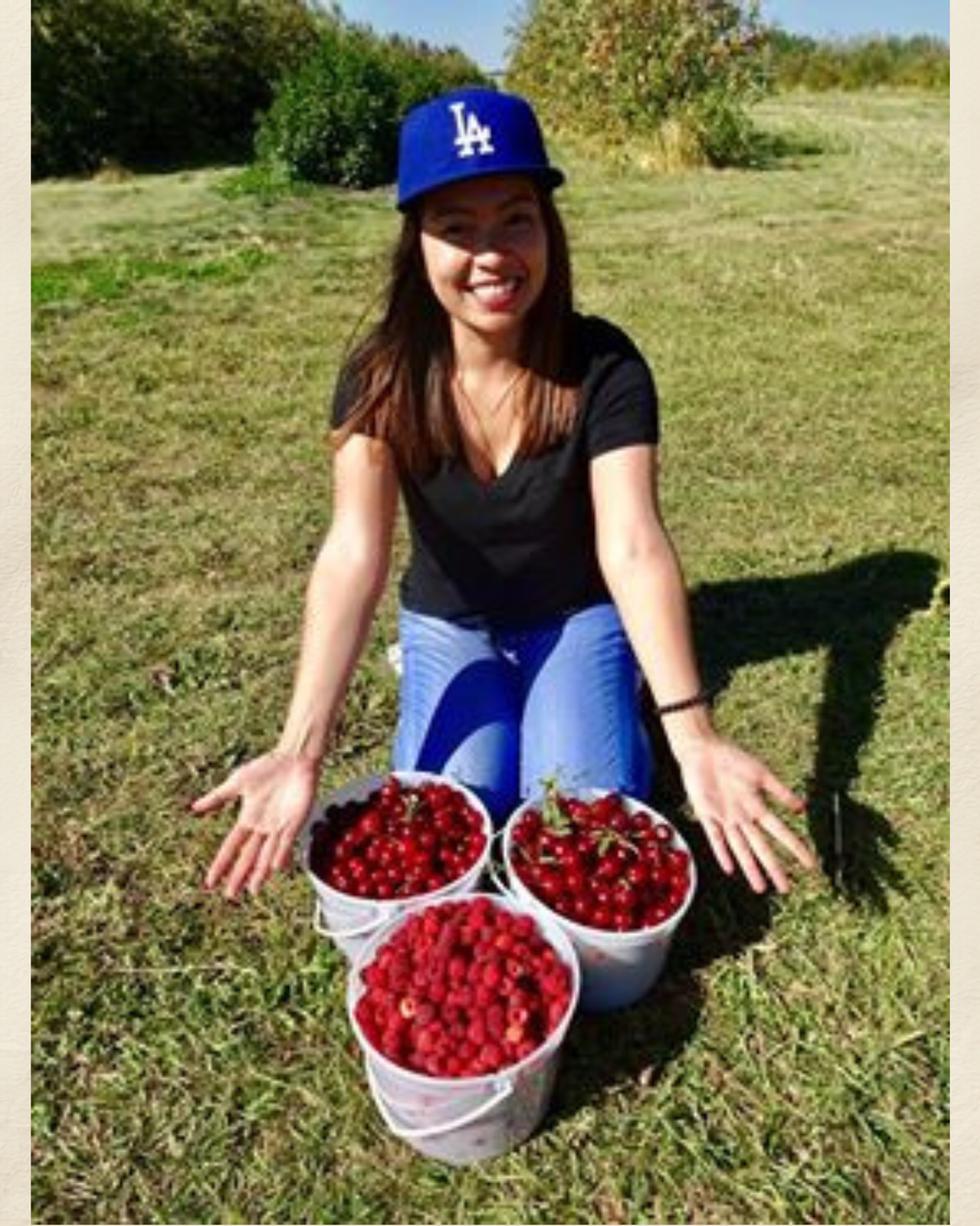 Person kneeling on grass behind three buckets filled with freshly picked red berries.