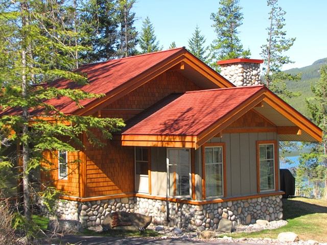 Forest cabin with red roof, lake view, and mountain backdrop.