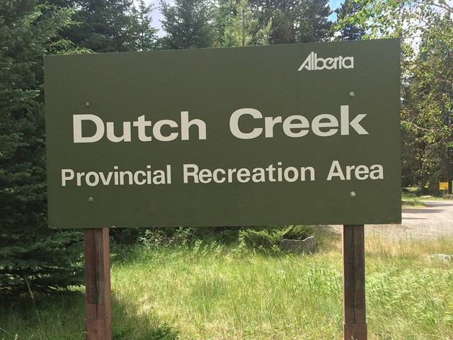 Dutch Creek Provincial Recreation Area sign with Alberta logo, surrounded by trees and grass.