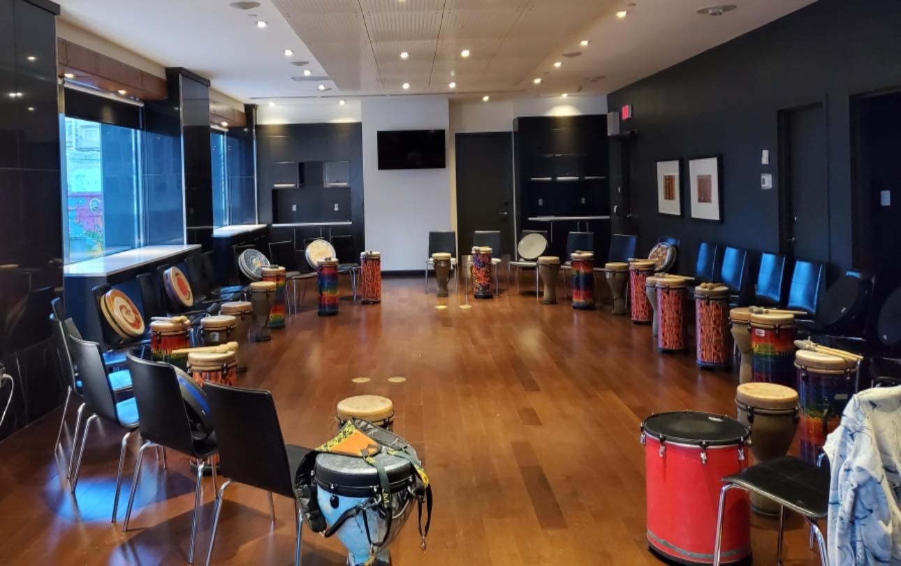 Indoor room with hand drums arranged in a circle, chairs around the space, and wooden floors set for Circles of Rhythm.