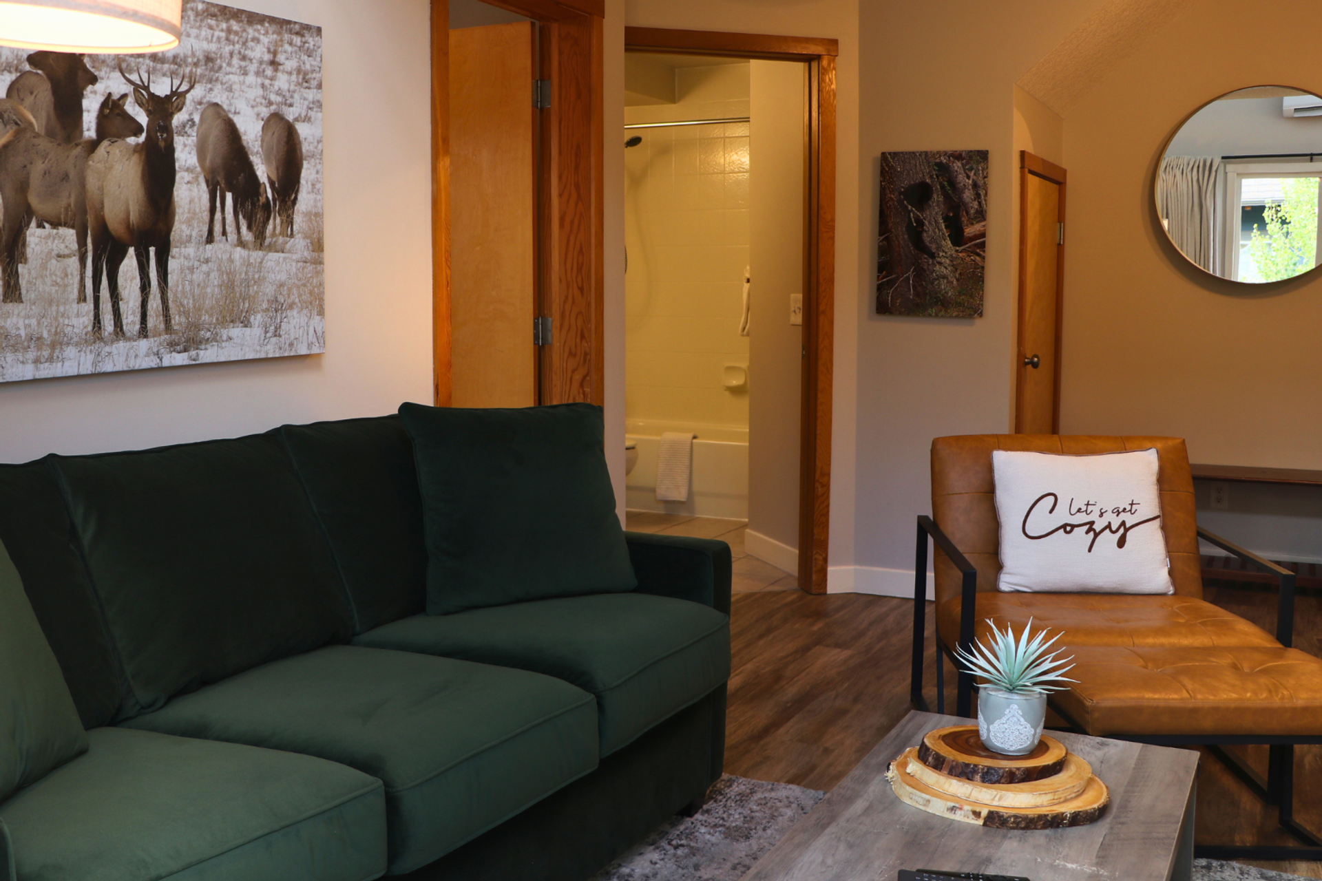 Living room with green sofa, leather chair, wildlife art and open bathroom doorway.