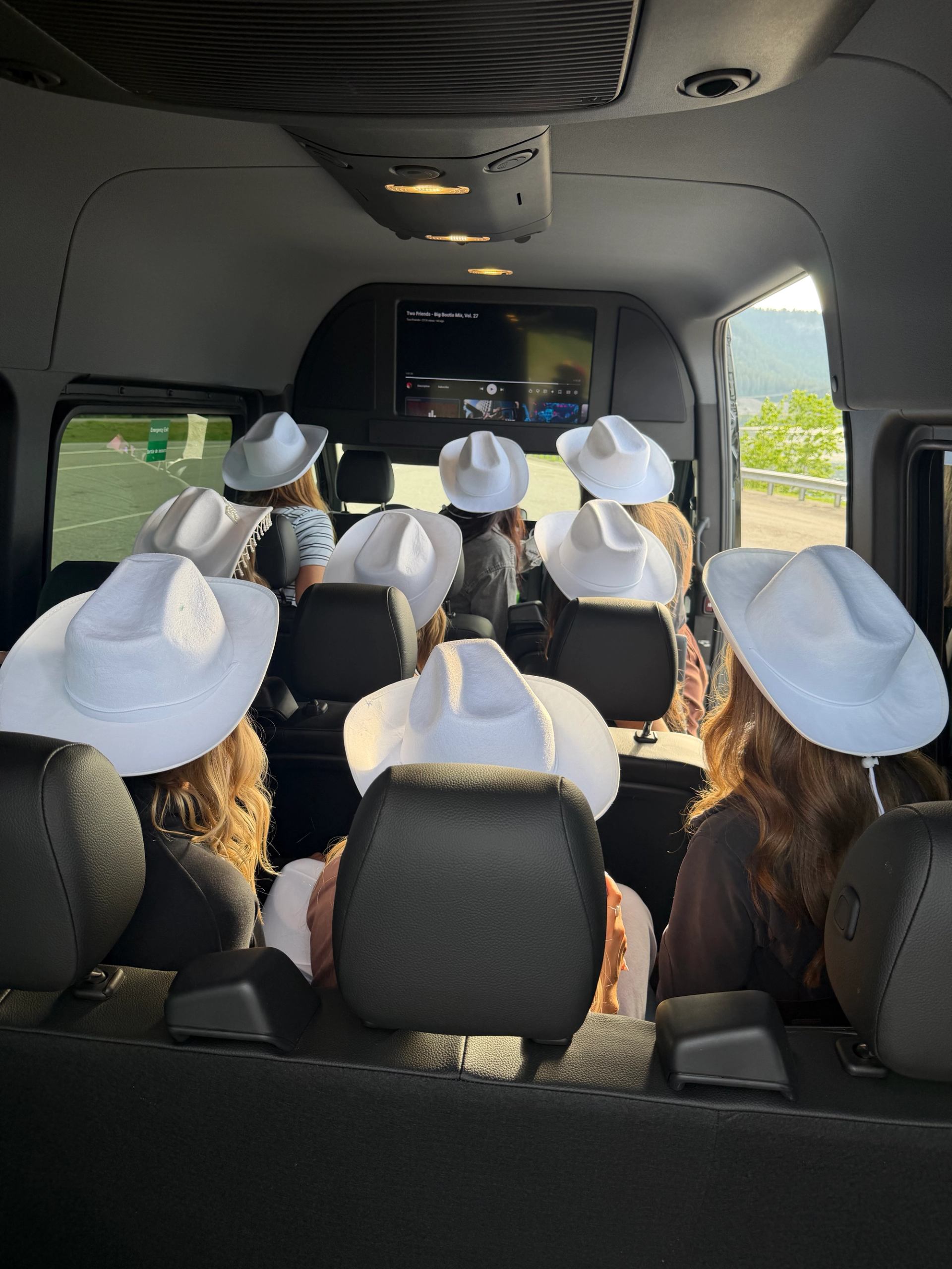 People wearing white cowboy hats sit in a van watching a screen ahead.