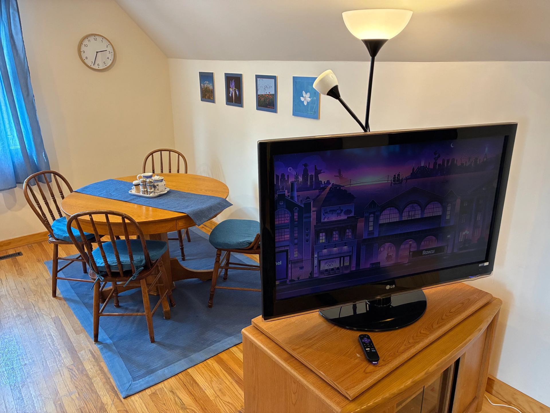 Dining area with wooden table, blue accents, wall art and television on cabinet.