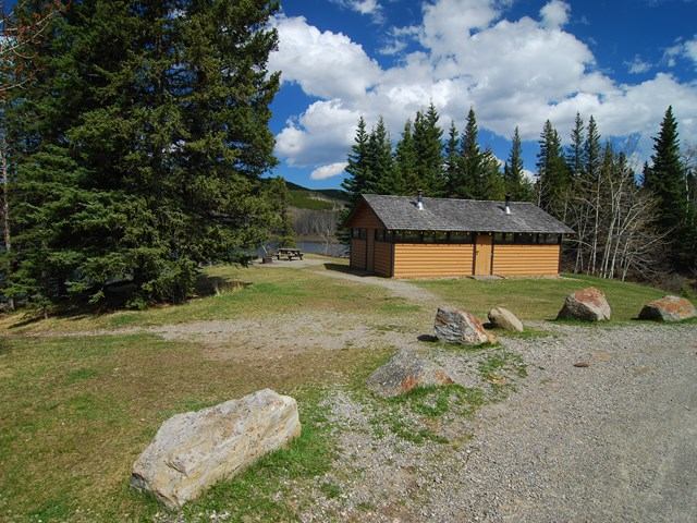 Cabin and gravel campsite beside Sibbald Lake, surrounded by pine trees and rocks.