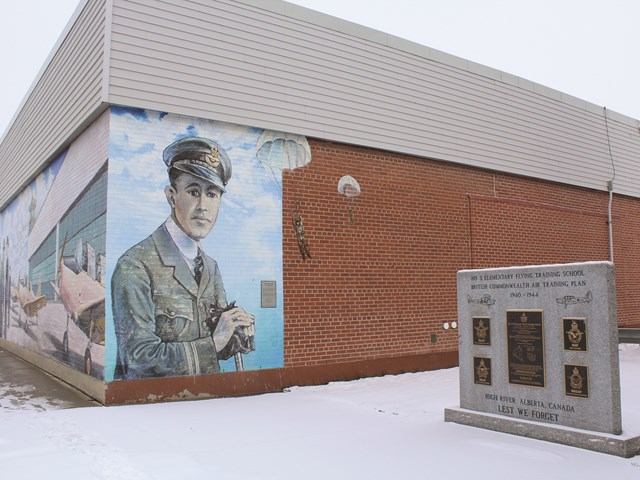 Mural of aviator with plane and parachute beside memorial stone in snowy High River.