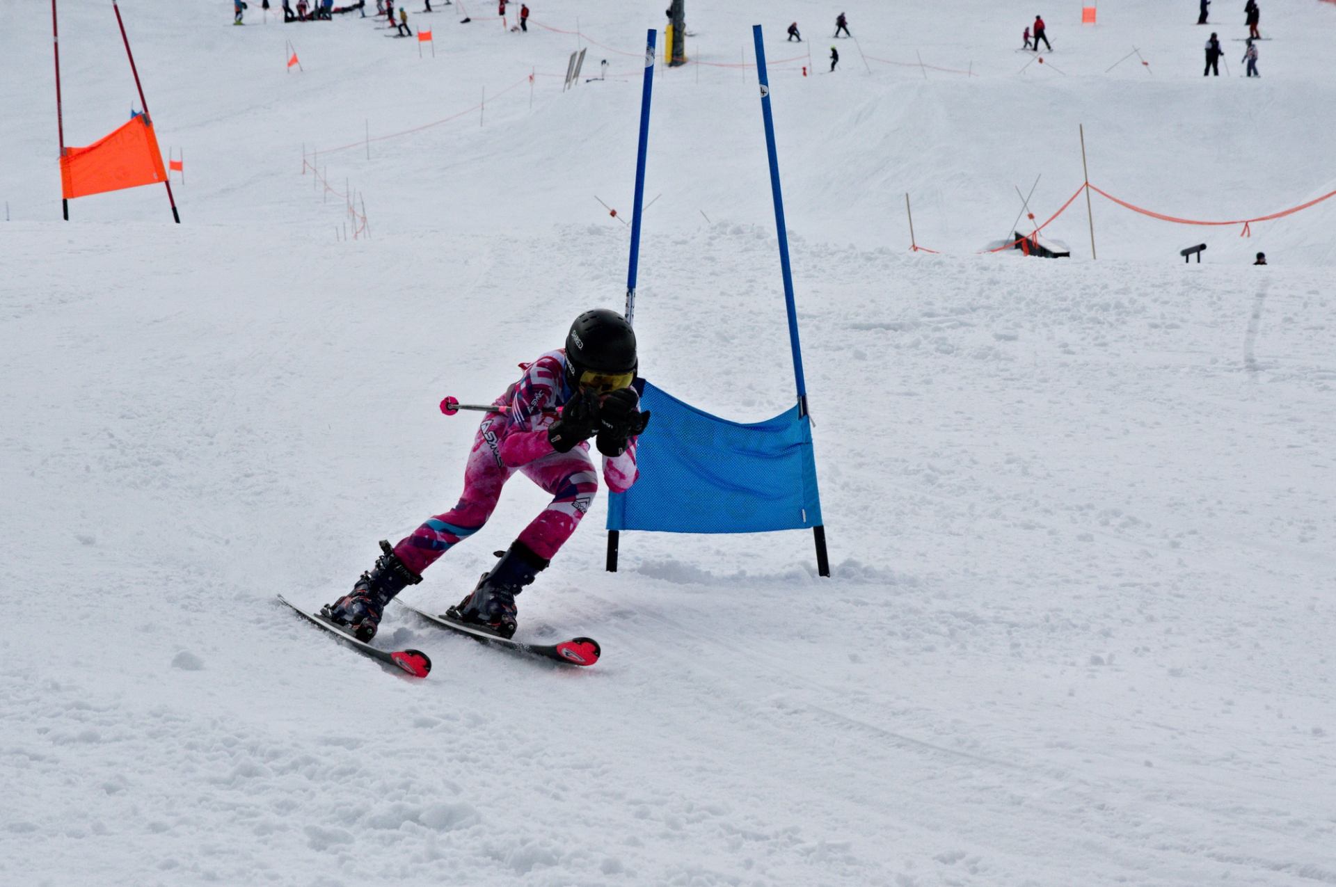 Skier in pink suit navigates a blue gate on a snowy race course.