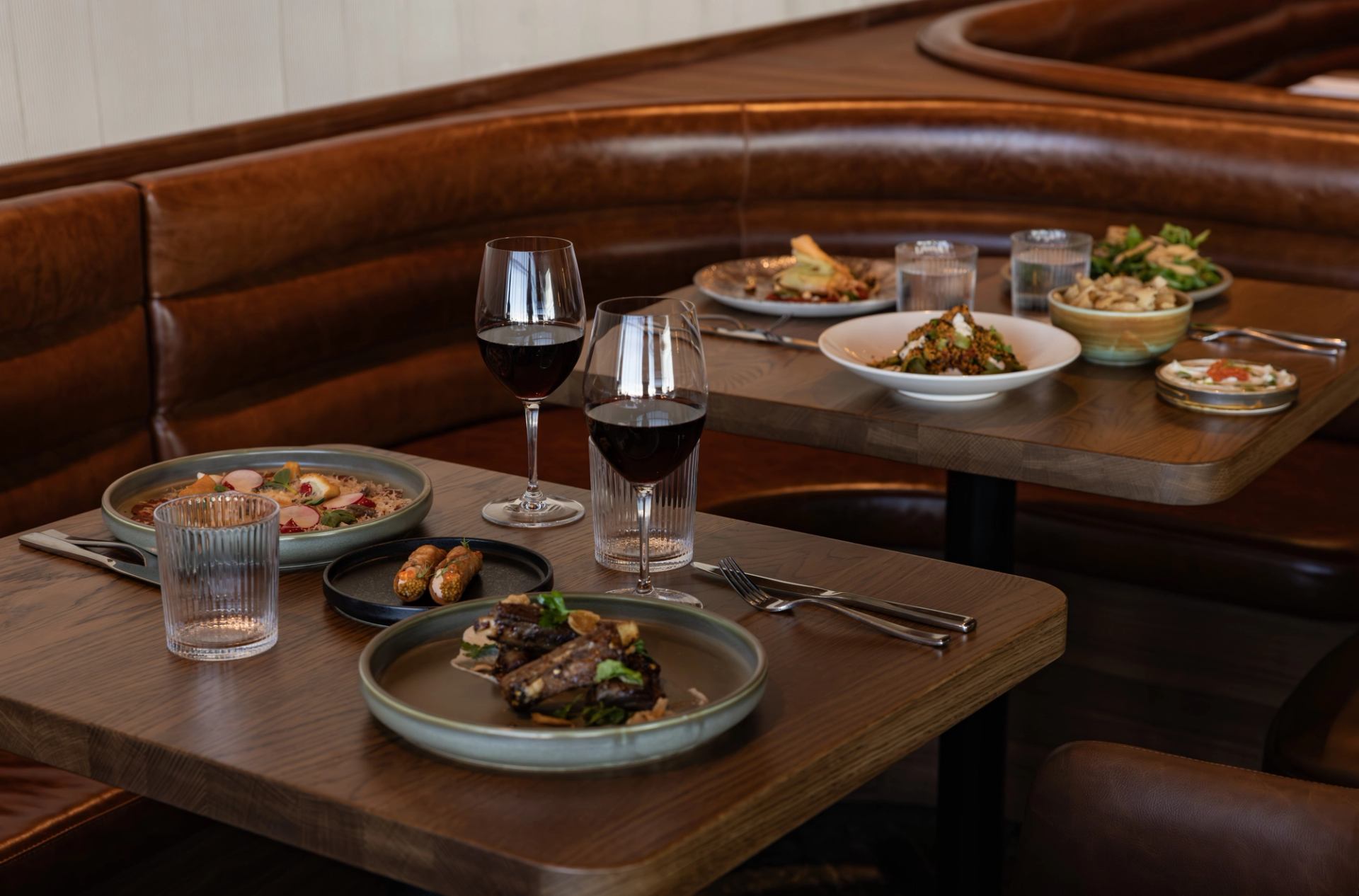 Restaurant table with plated dishes, two glasses of red wine and water glasses.
