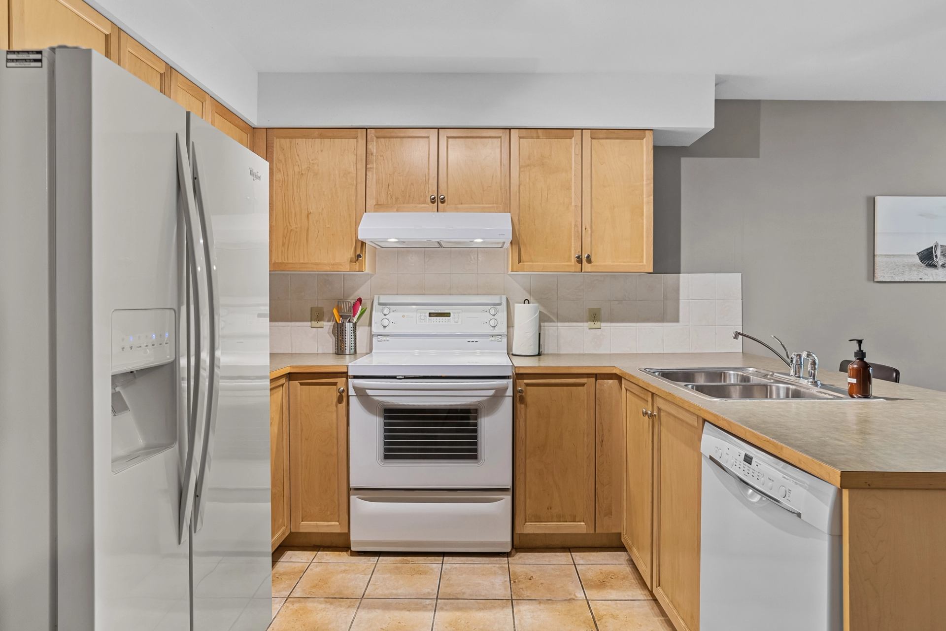Kitchen with stainless steel fridge, oven, dishwasher, wood cabinets, and tiled floor.