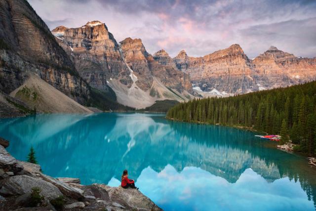 An aerial view of a person sitting on a cliff overlooking Moraine Lake in Banff National Park.