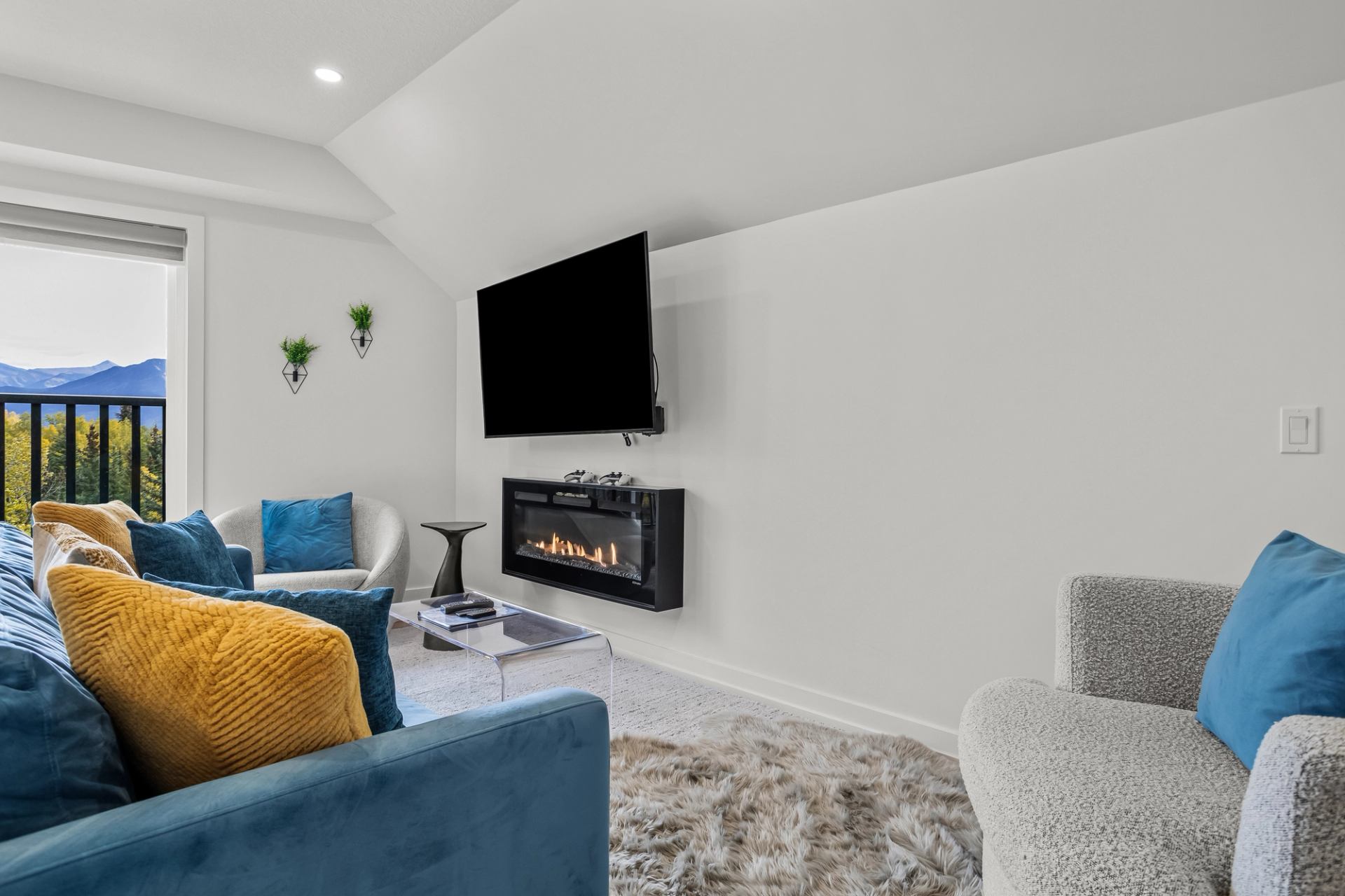 Living room with blue sofa, wall-mounted TV, electric fireplace and mountain view.